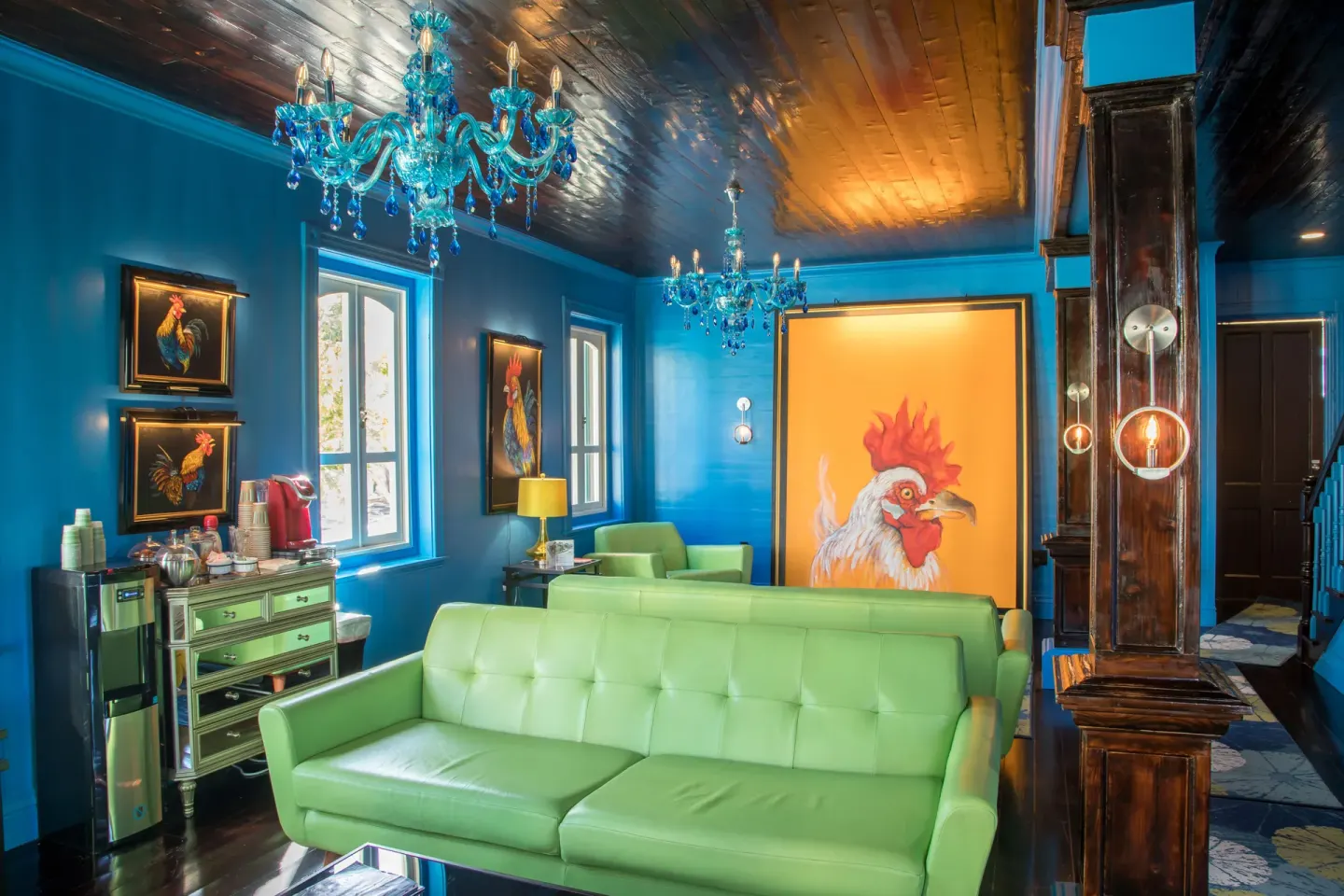 Colorful lounge with green sofas, blue chandeliers, and rooster artwork at The Fred.