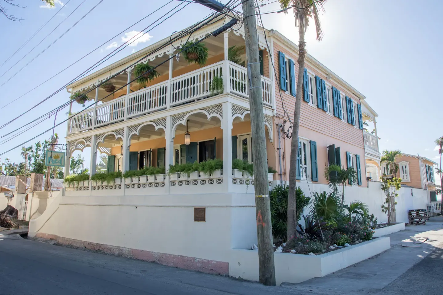 Corner street view of The Fred with white balconies, teal shutters, palms, and overhead wires.