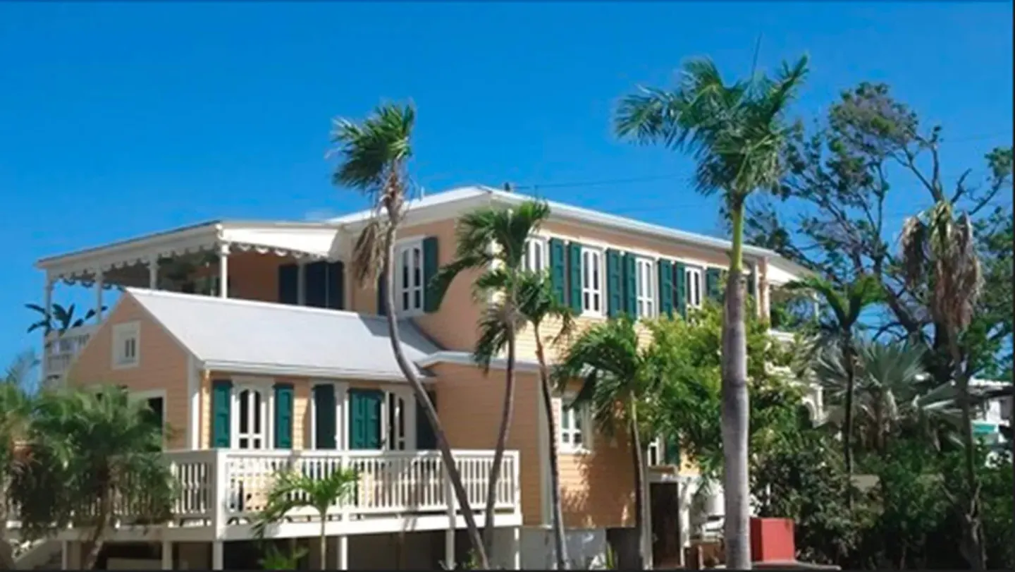 Exterior of The Fred with peach walls, teal shutters, white railings, and palm trees.