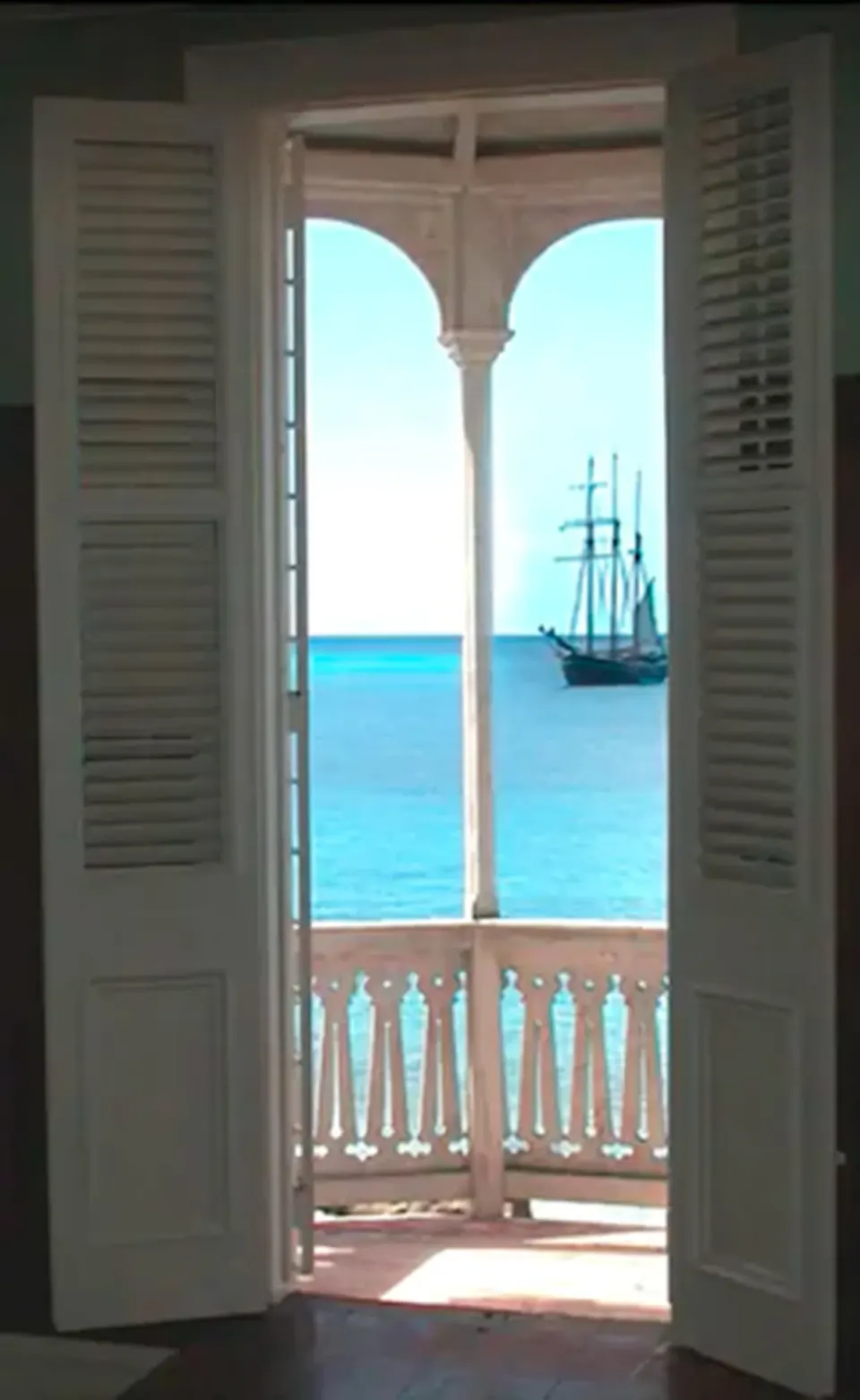 Open shutters in the Rachel room at The Fred frame a balcony and blue sea.