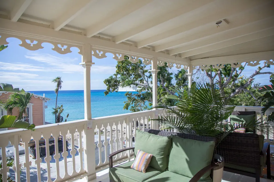 Balcony at The Fred with cushioned chairs, white railing, trees, and a blue sea view.