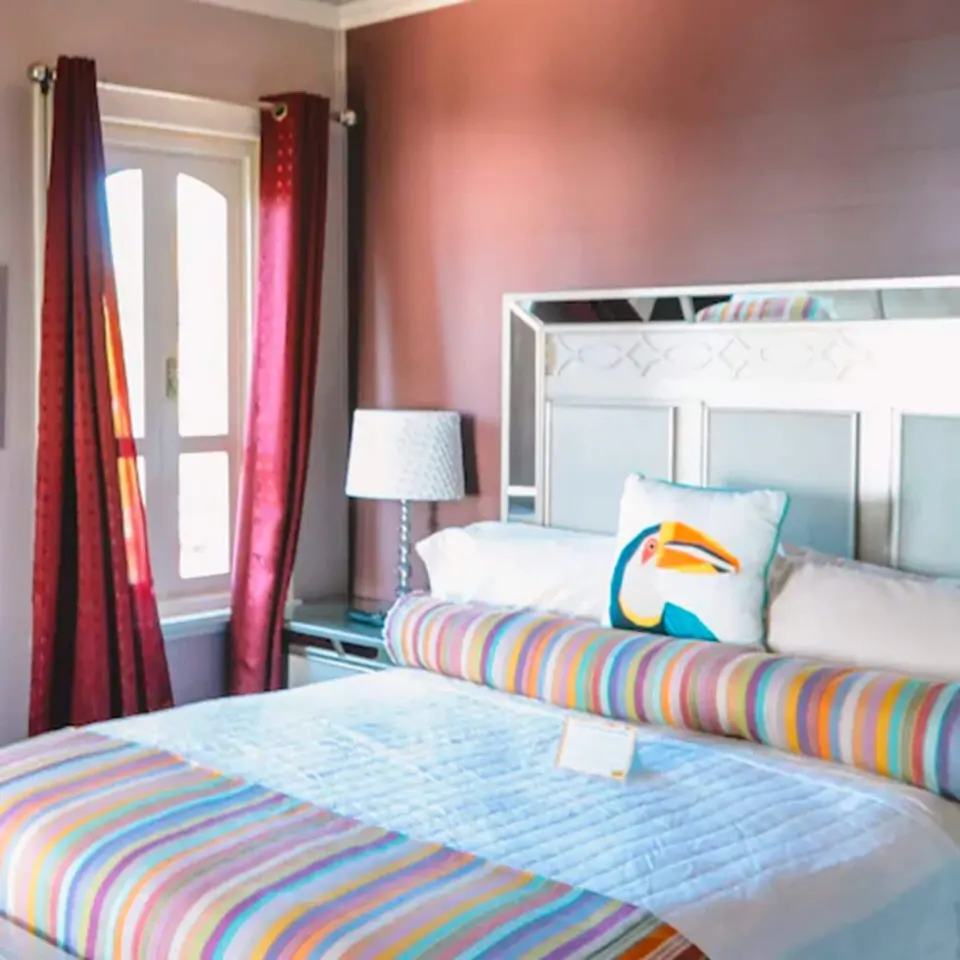 Romantic Room at The Fred with bed, striped bolster, toucan pillow, bedside lamp, and window.