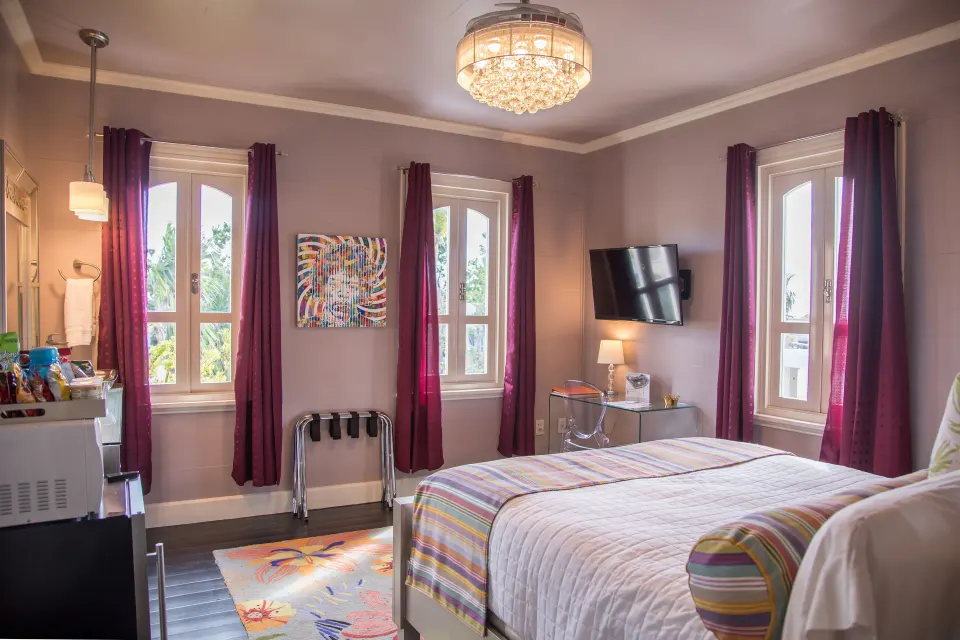 Romantic Room at The Fred with bed, burgundy curtains, chandelier, wall TV, and tall windows.