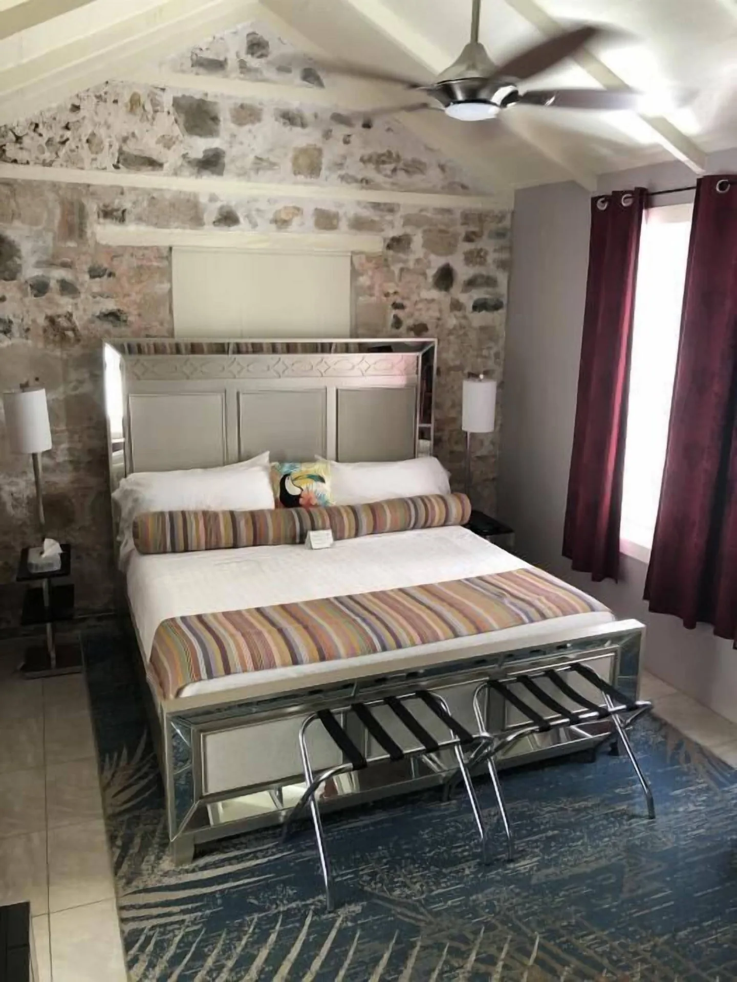 King bed in the Madison guest room at The Fred with stone wall, vaulted ceiling, and burgundy curtains.
