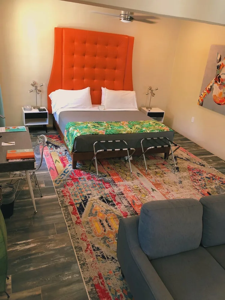 Signature Room at The Fred showing a king bed, orange headboard, luggage benches, and sofa.