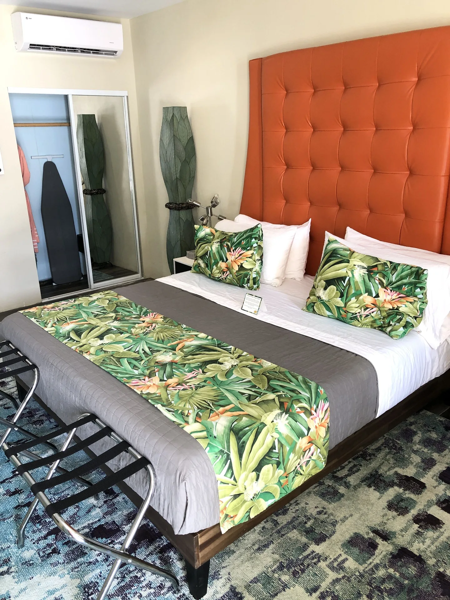 Signature Room at The Fred with king bed, orange tufted headboard, mirrored closet, and luggage racks.