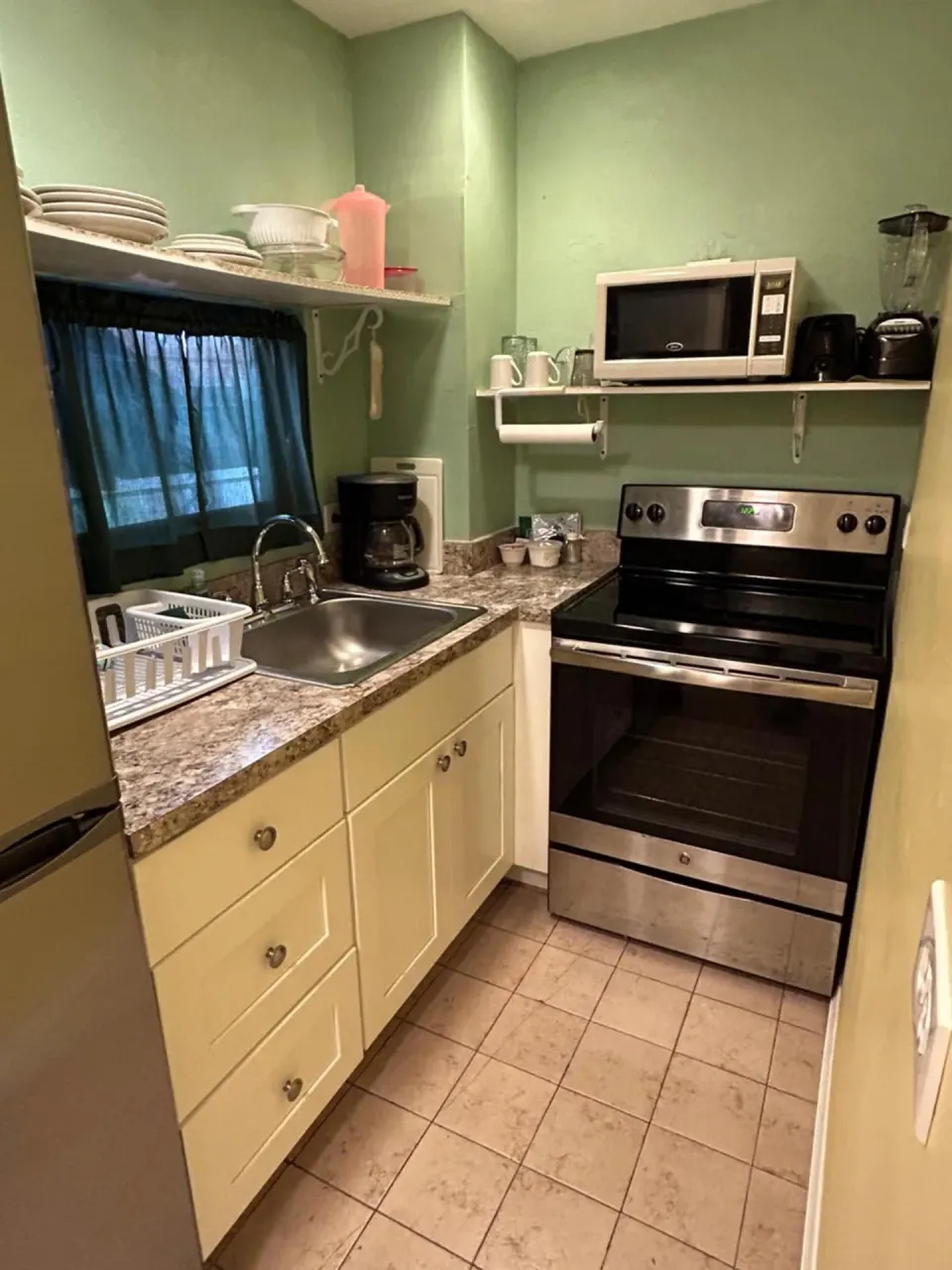 Compact kitchenette with stove, sink, microwave, and shelves at The Green Iguana Hotel.