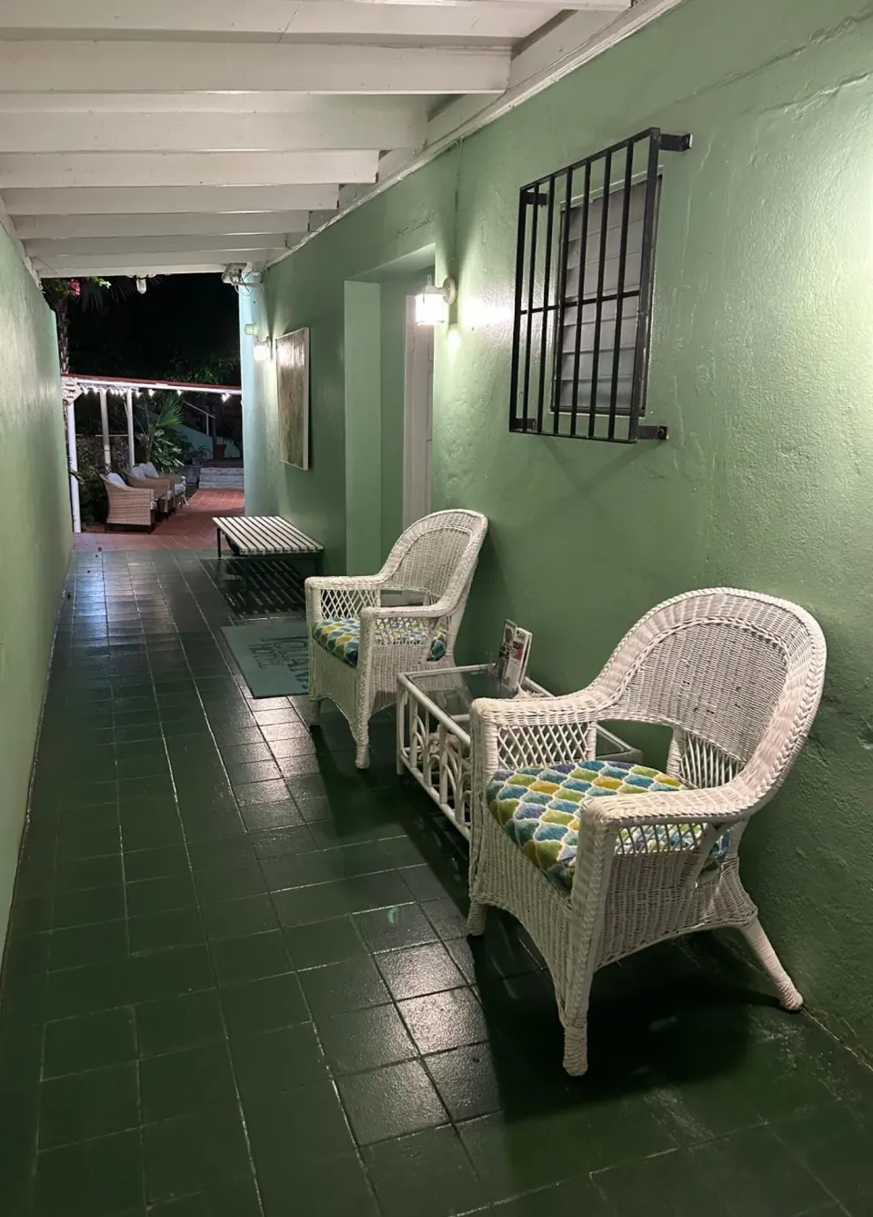 Covered corridor with wicker chairs and green tile floor at The Green Iguana Hotel.