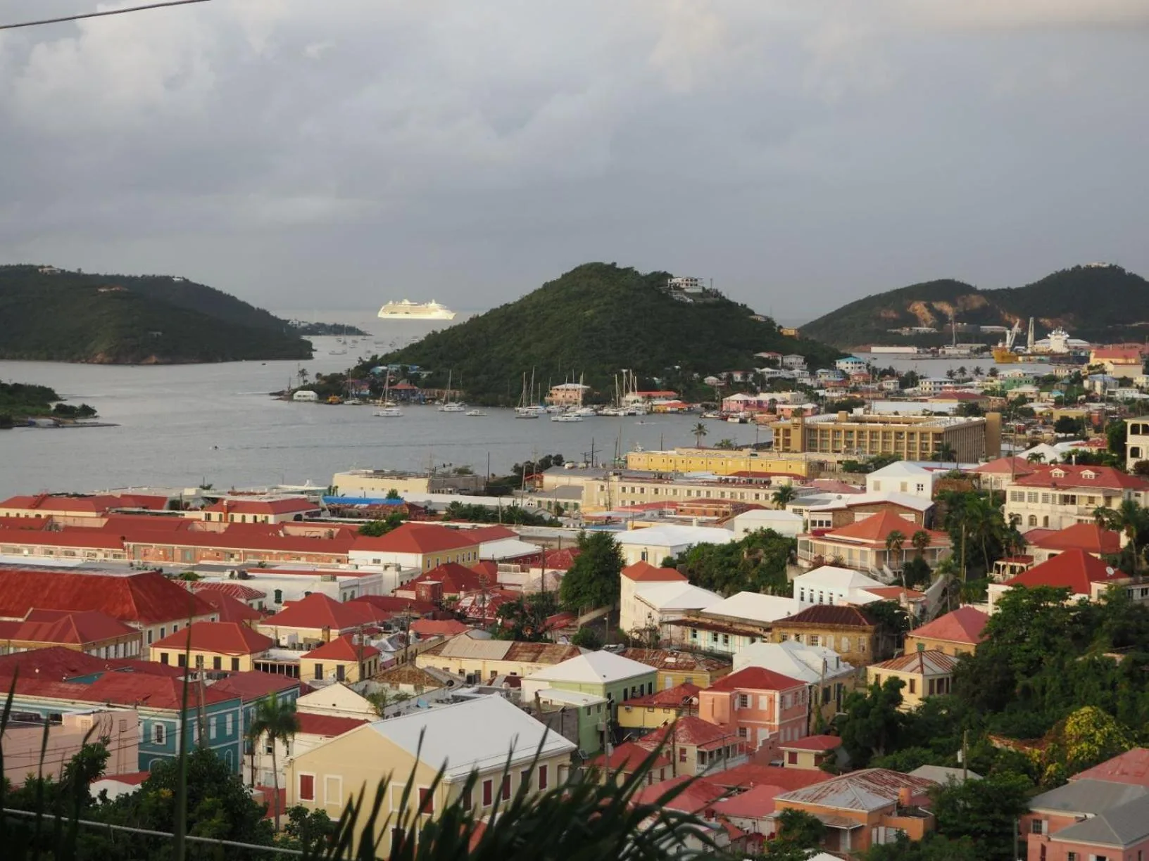 Daytime harbor view with red roofs, hills, and boats near The Green Iguana Hotel.
