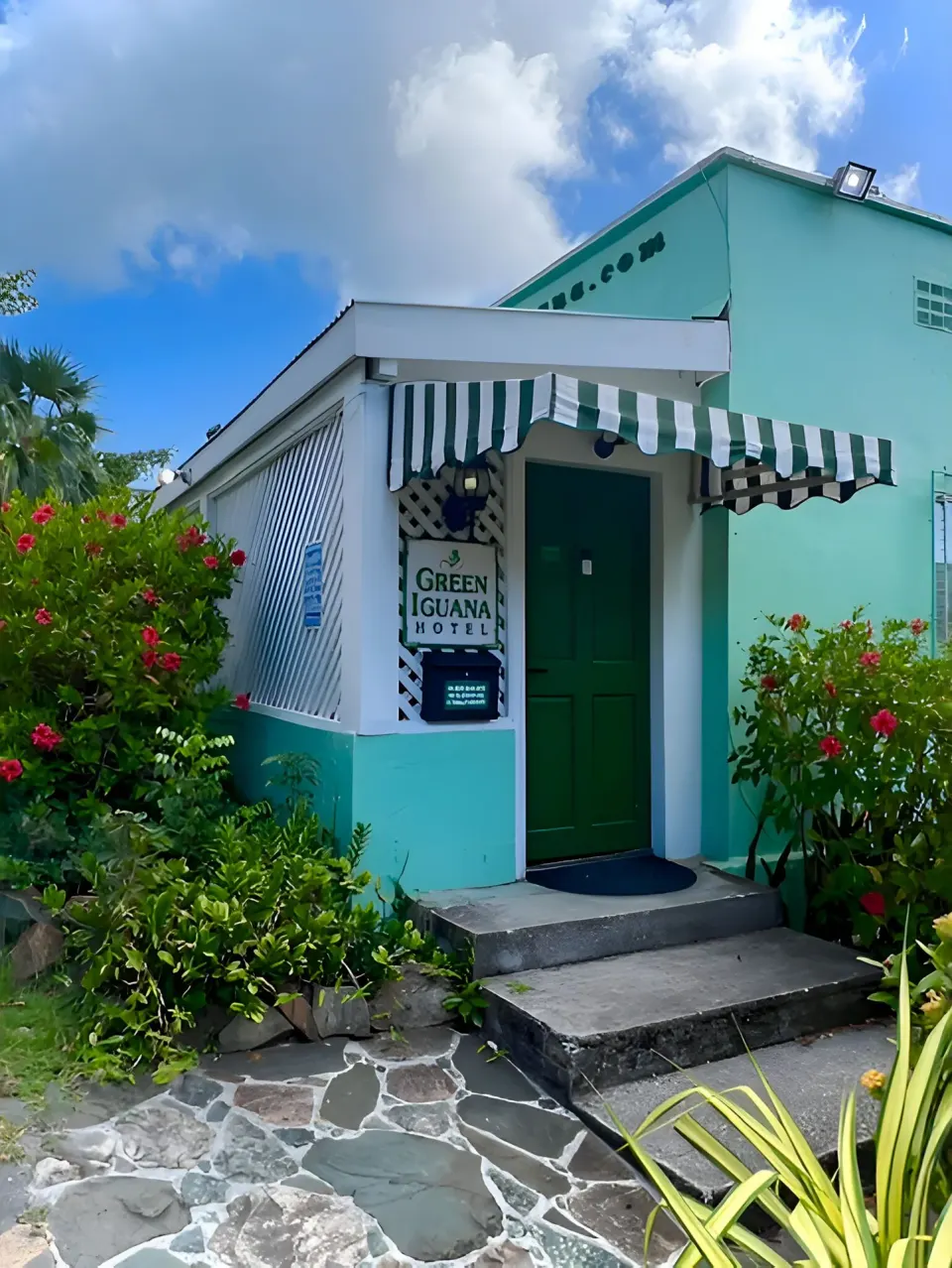 Hotel entrance with striped awning and tropical plants at The Green Iguana Hotel.