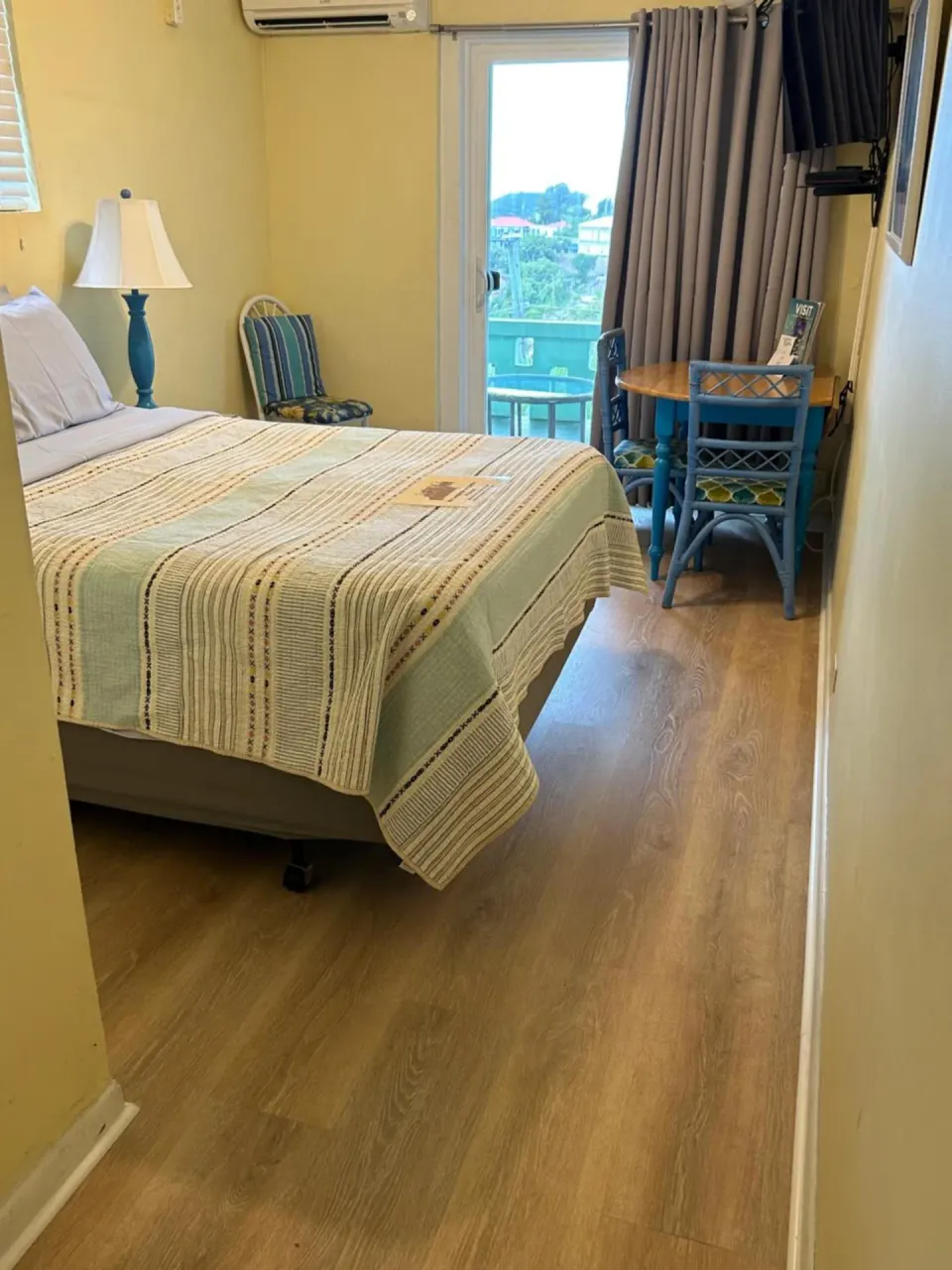 Guest room with bed, blue table, and balcony door at The Green Iguana Hotel.