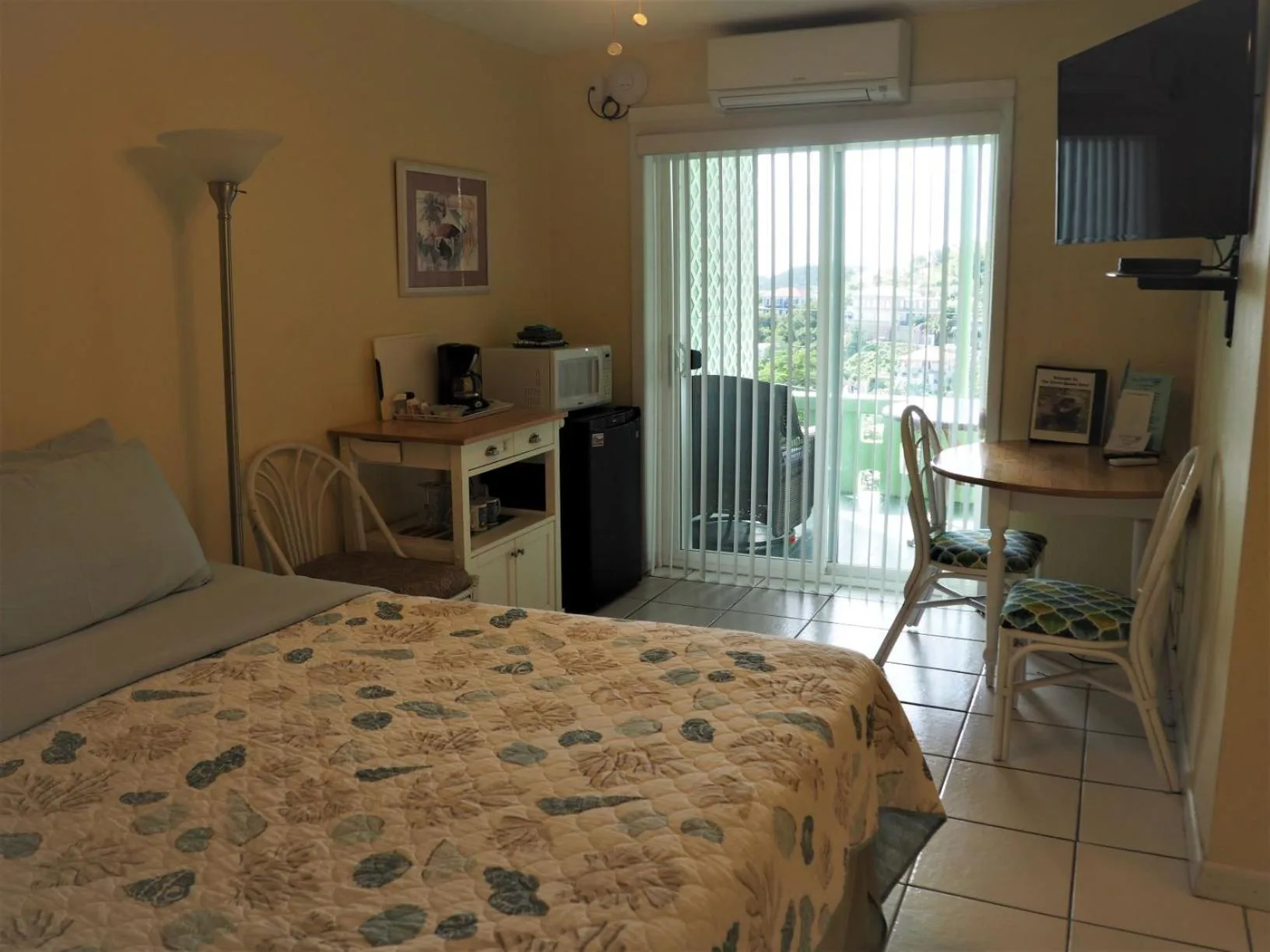 Guest room with bed, kitchenette, dining table, and balcony doors at The Green Iguana Hotel.