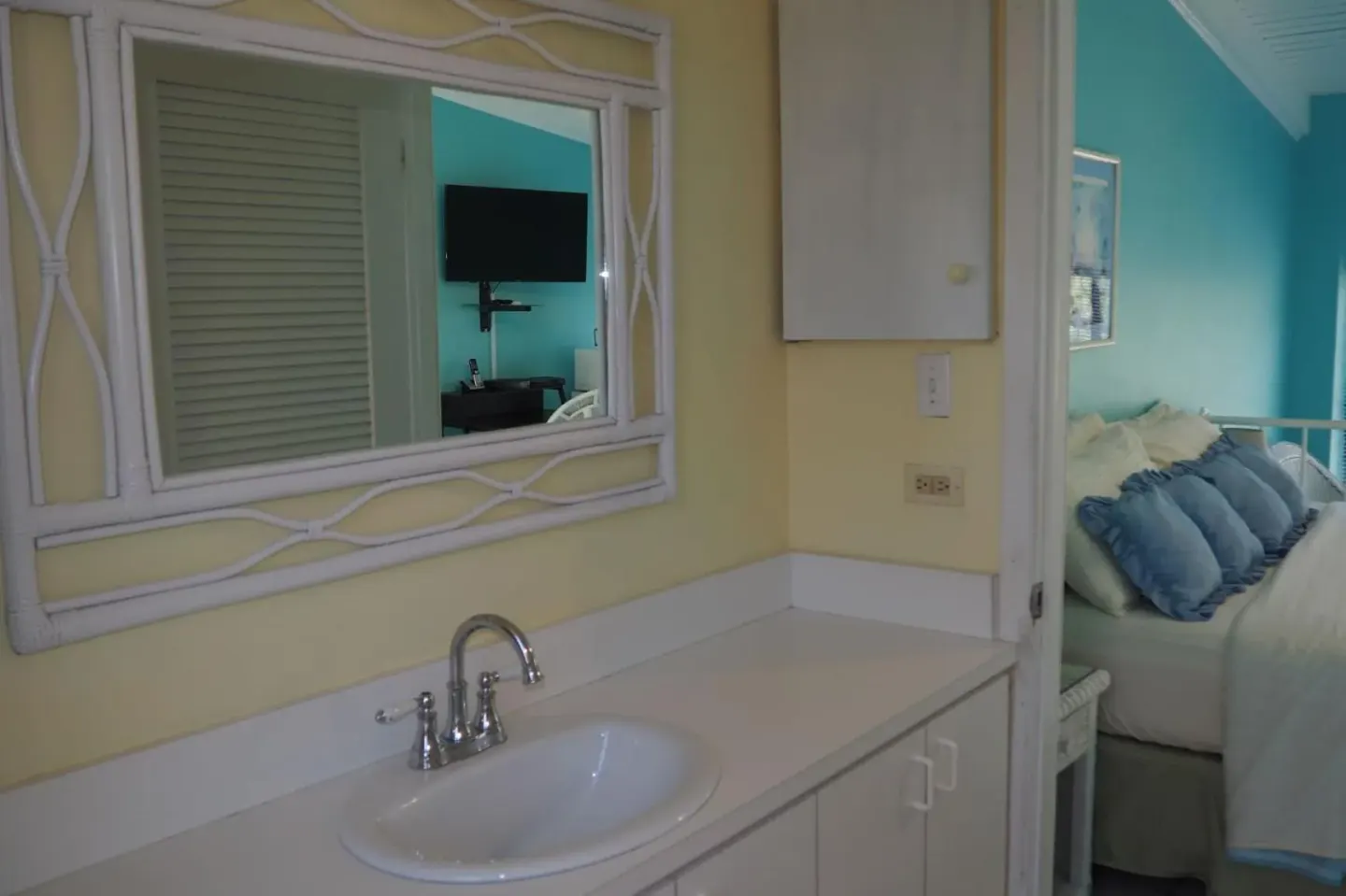 Vanity with sink and mirror beside a turquoise bedroom at The Green Iguana Hotel.