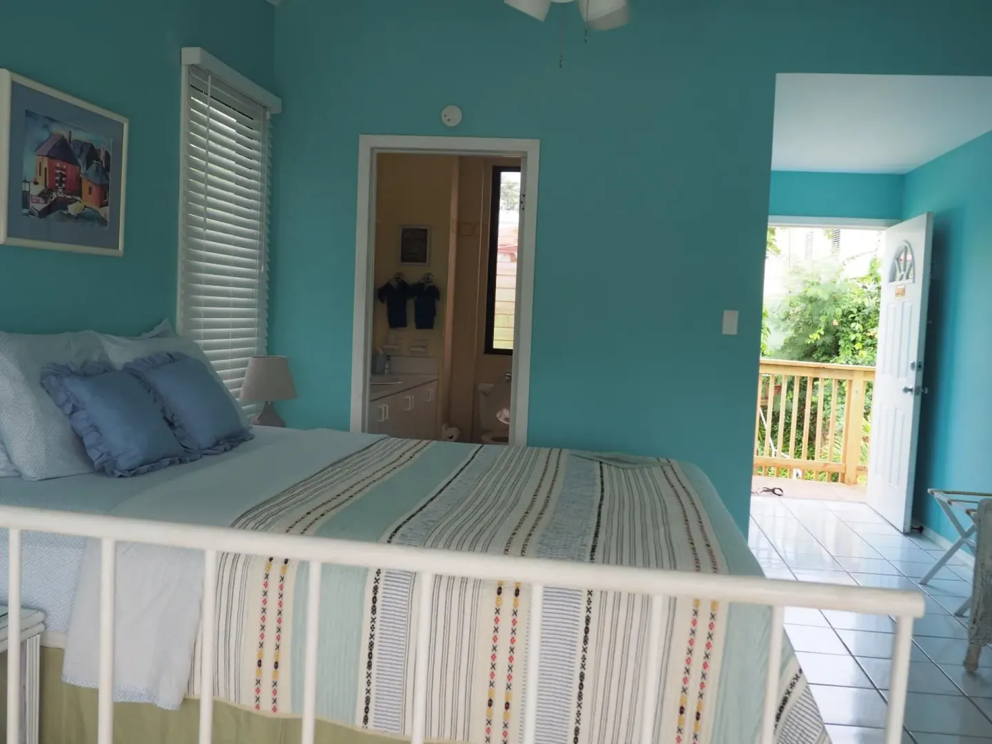 Turquoise guest room with white bed and open balcony door at The Green Iguana Hotel.