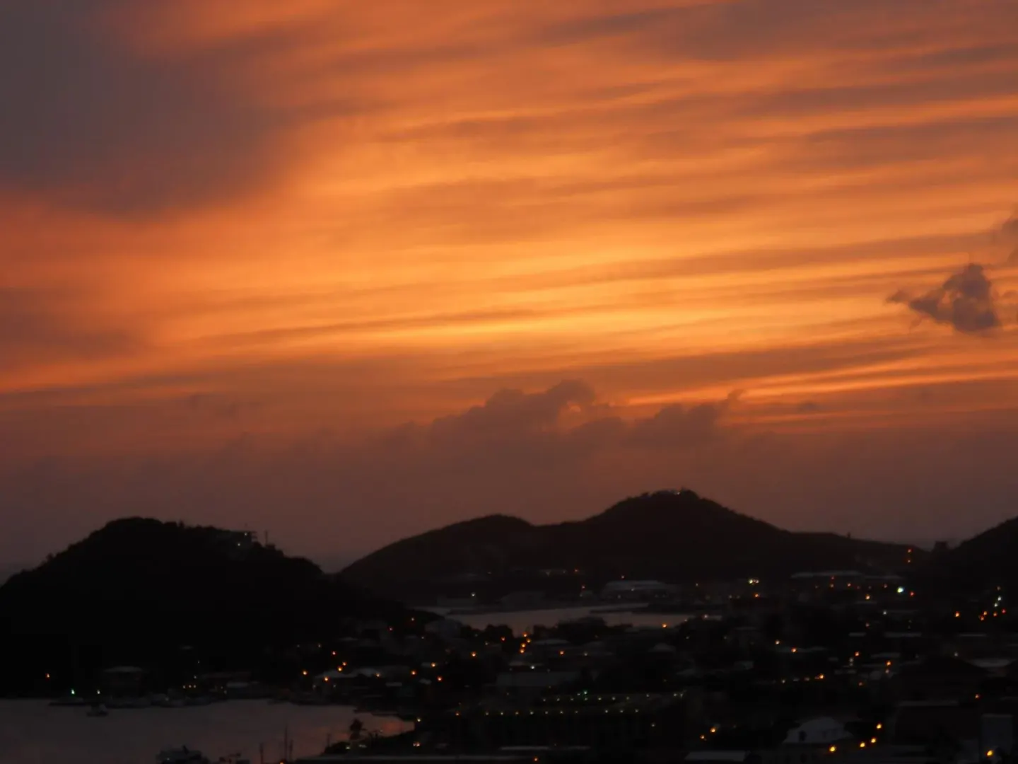 Orange sunset over hills, harbor, and town lights near The Green Iguana Hotel.