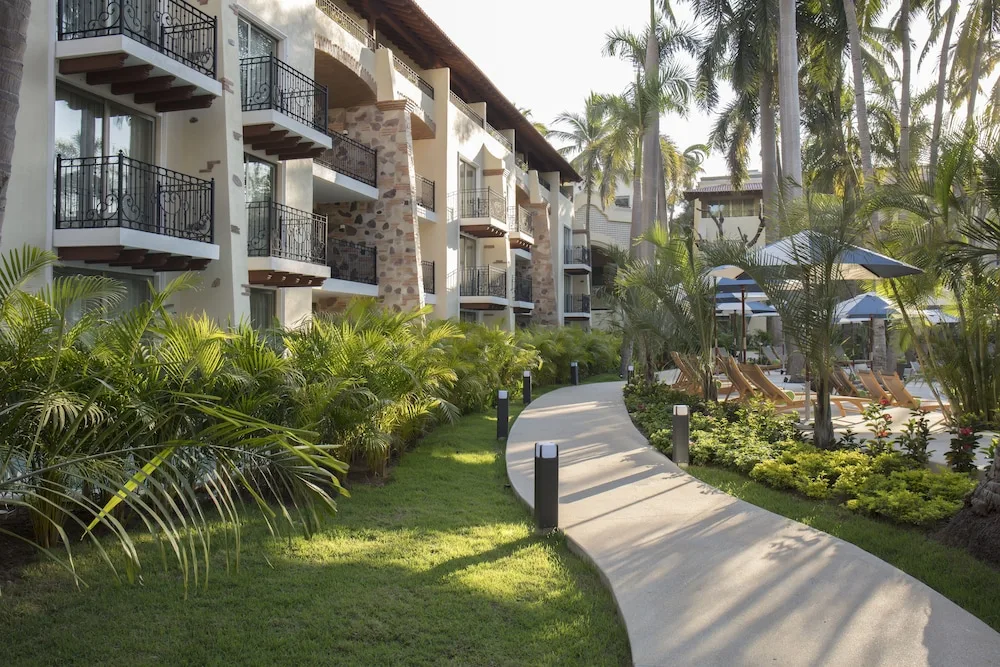 Curved garden walkway by balconies and pool umbrellas at The Hacienda at Krystal Grand Puerto Vallarta.