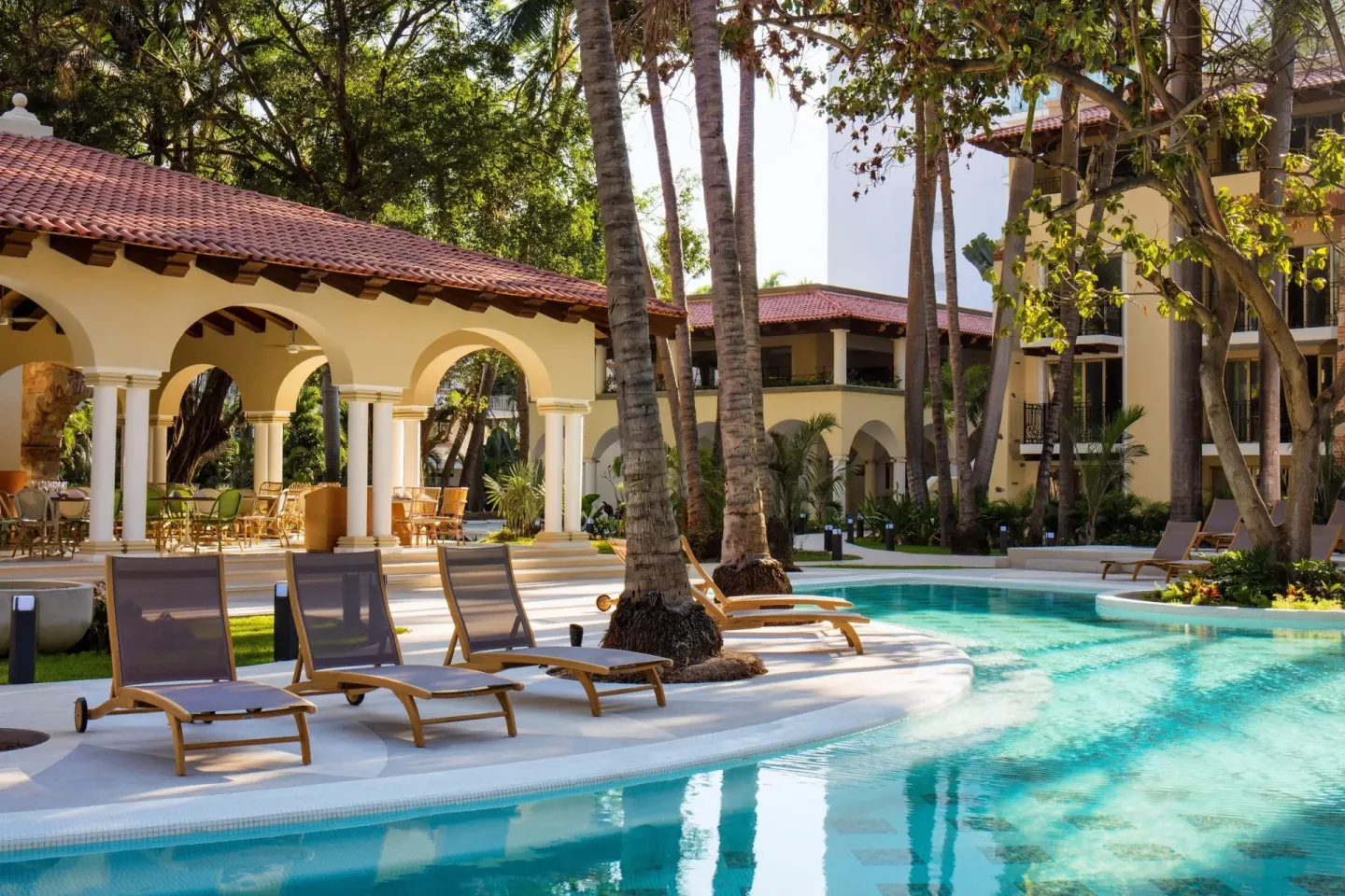 Curving pool with loungers, palms, and arched terrace at The Hacienda at Krystal Grand Puerto Vallarta.