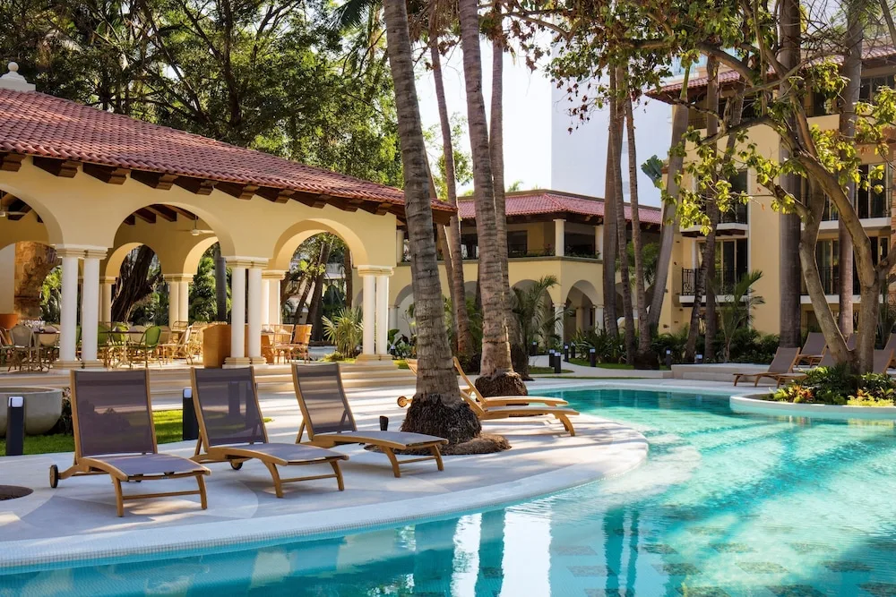 Poolside loungers beneath palms at The Hacienda at Krystal Grand Puerto Vallarta.