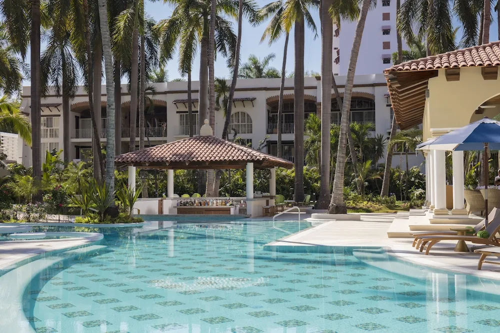 Resort pool with palms and tiled-roof pavilion at The Hacienda at Krystal Grand Puerto Vallarta.
