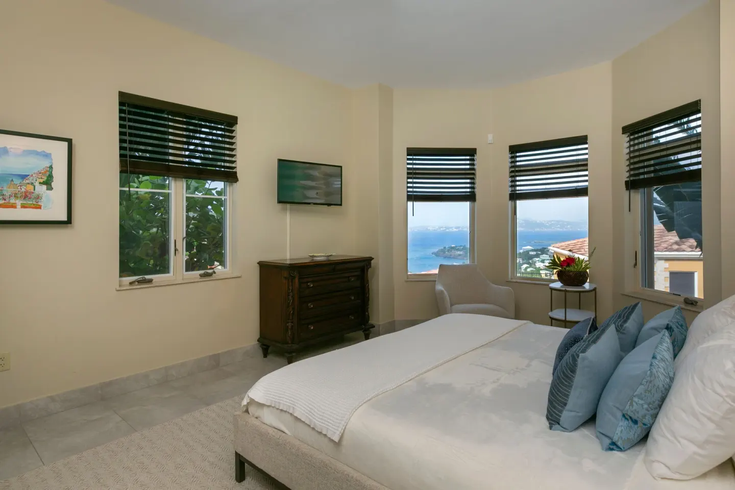 King bedroom with dark blinds, dresser, TV, and ocean-view windows at The Hills, St John.