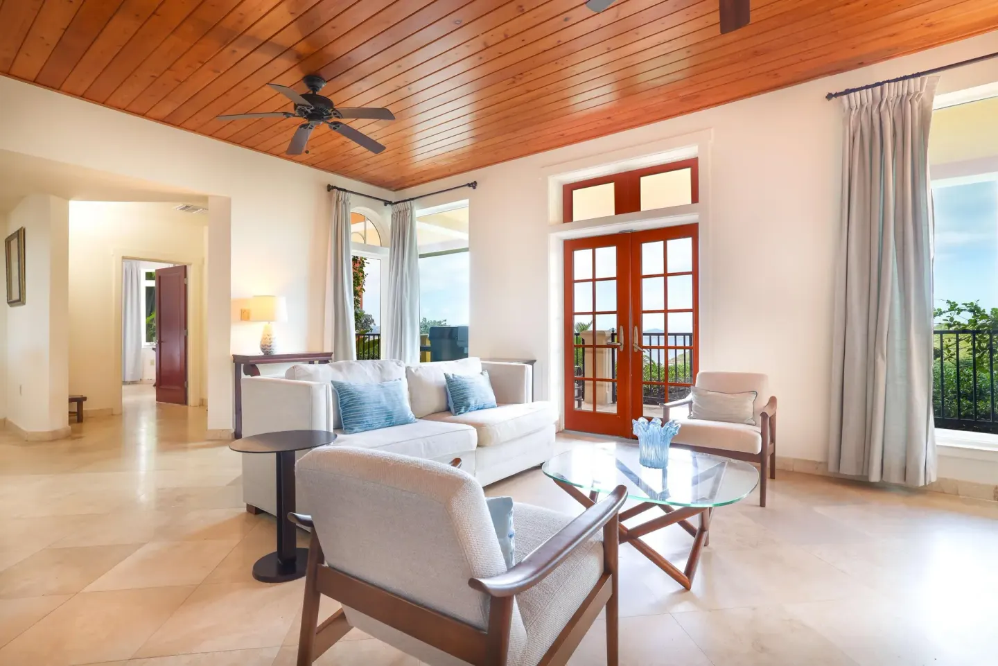 Living room with white seating, glass table, red doors, and balcony views at The Hills, St John.