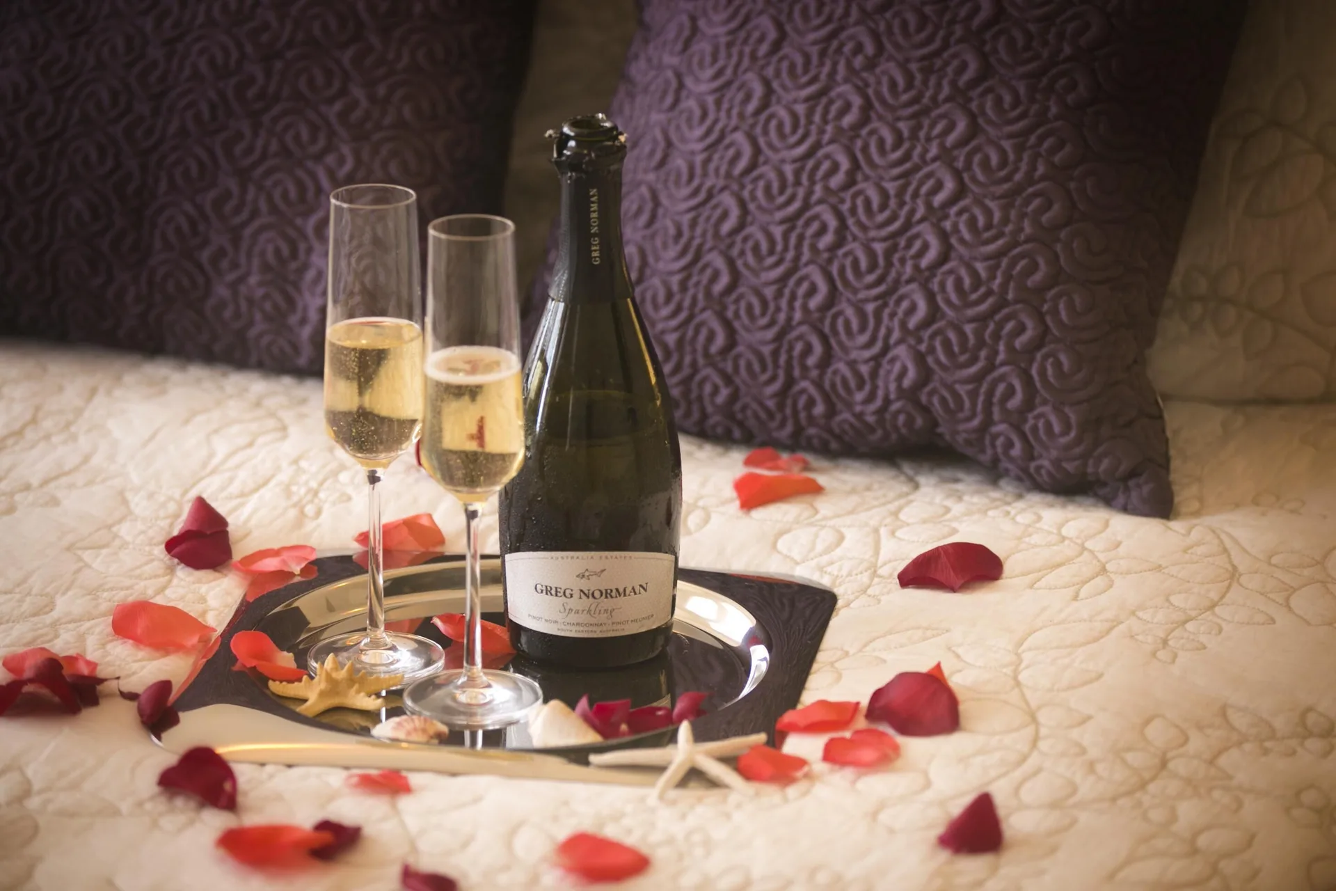 Sparkling wine, glasses, rose petals, and shells on a bed at The Hills, St John.