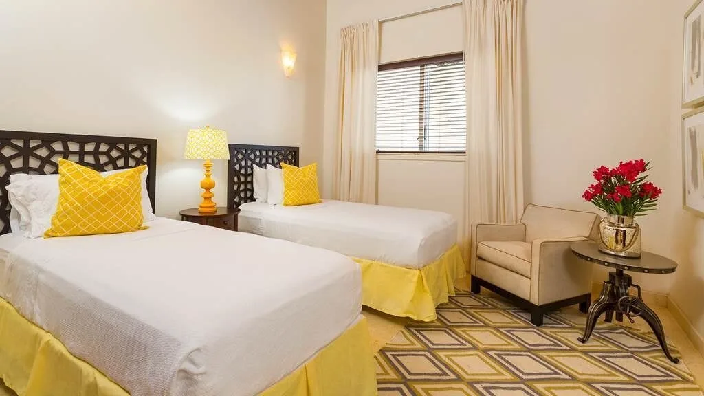 Twin bedroom with yellow accents, armchair, and side table flowers at The Hills, St John.