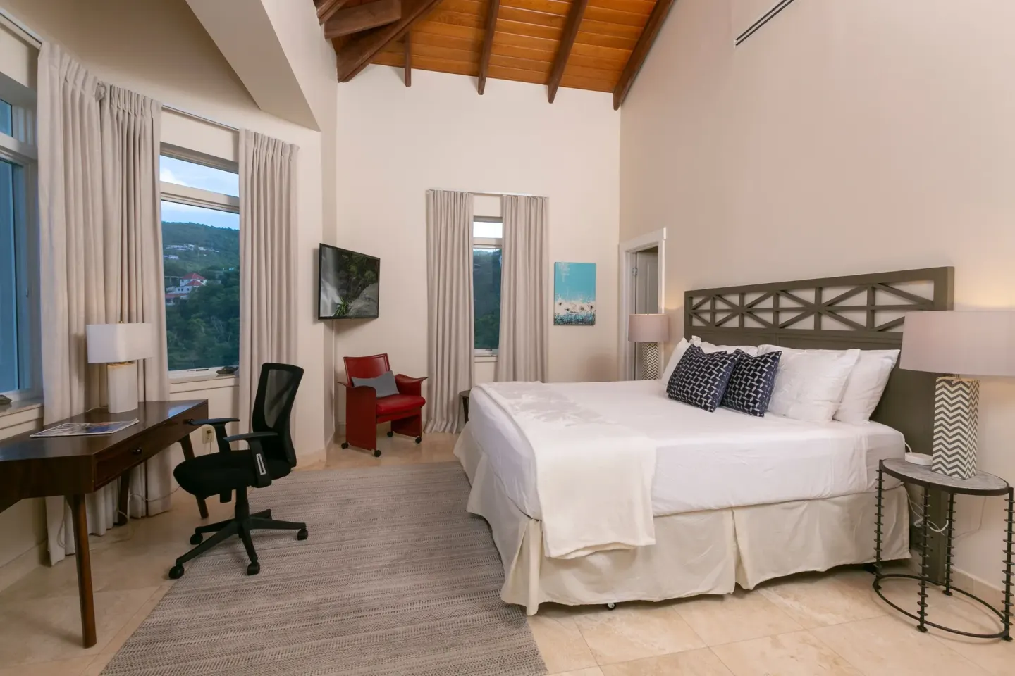 King bedroom with desk, red chair, wall TV, and vaulted wood ceiling at The Hills, St John.