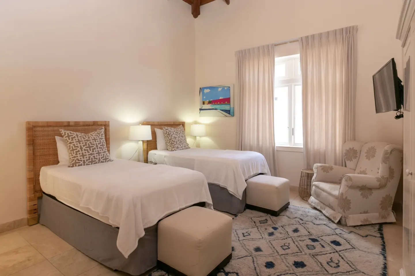Twin bedroom with woven headboards, ottomans, armchair, and wall TV at The Hills, St John.
