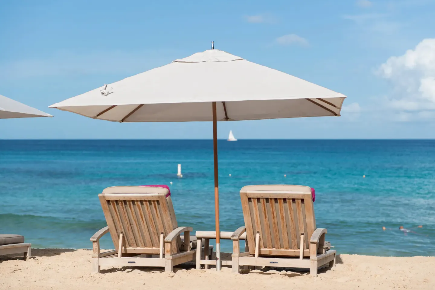 Two wooden beach chairs under a white umbrella facing the sea at The House.