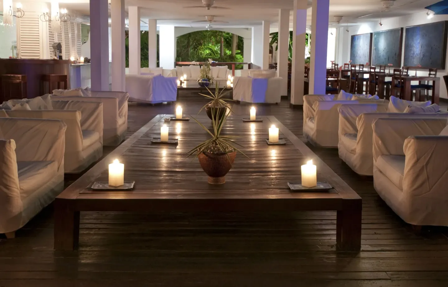 Candlelit lounge with white sofas and a long wooden table at The House.