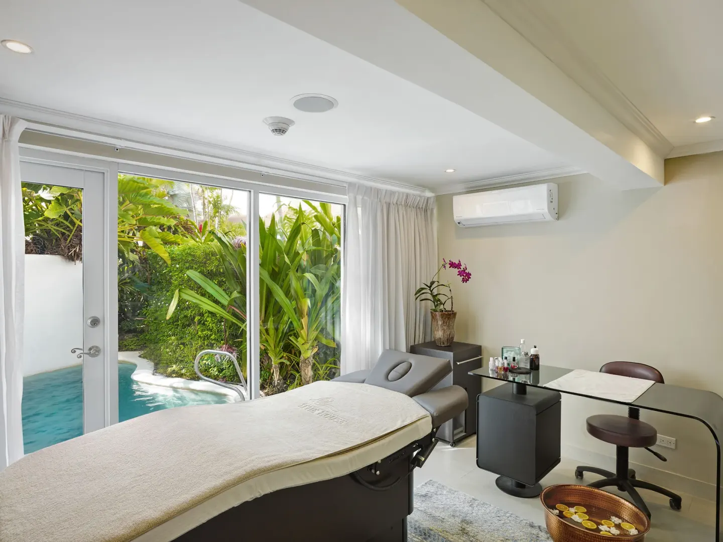 Spa treatment room with massage bed, garden pool view and workstation at The House.