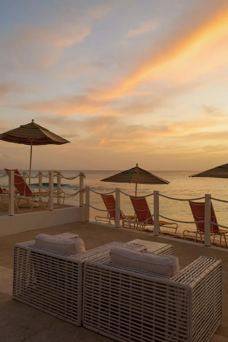 Wicker lounge seating overlooks beach umbrellas and sunset at The House.