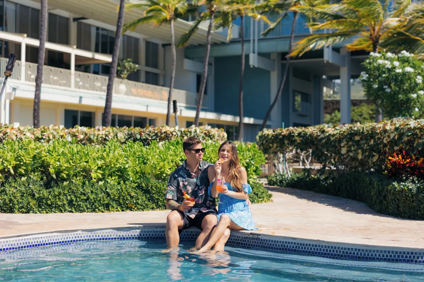 Couple sitting at the pool edge with drinks at The Kahala Hotel & Resort.