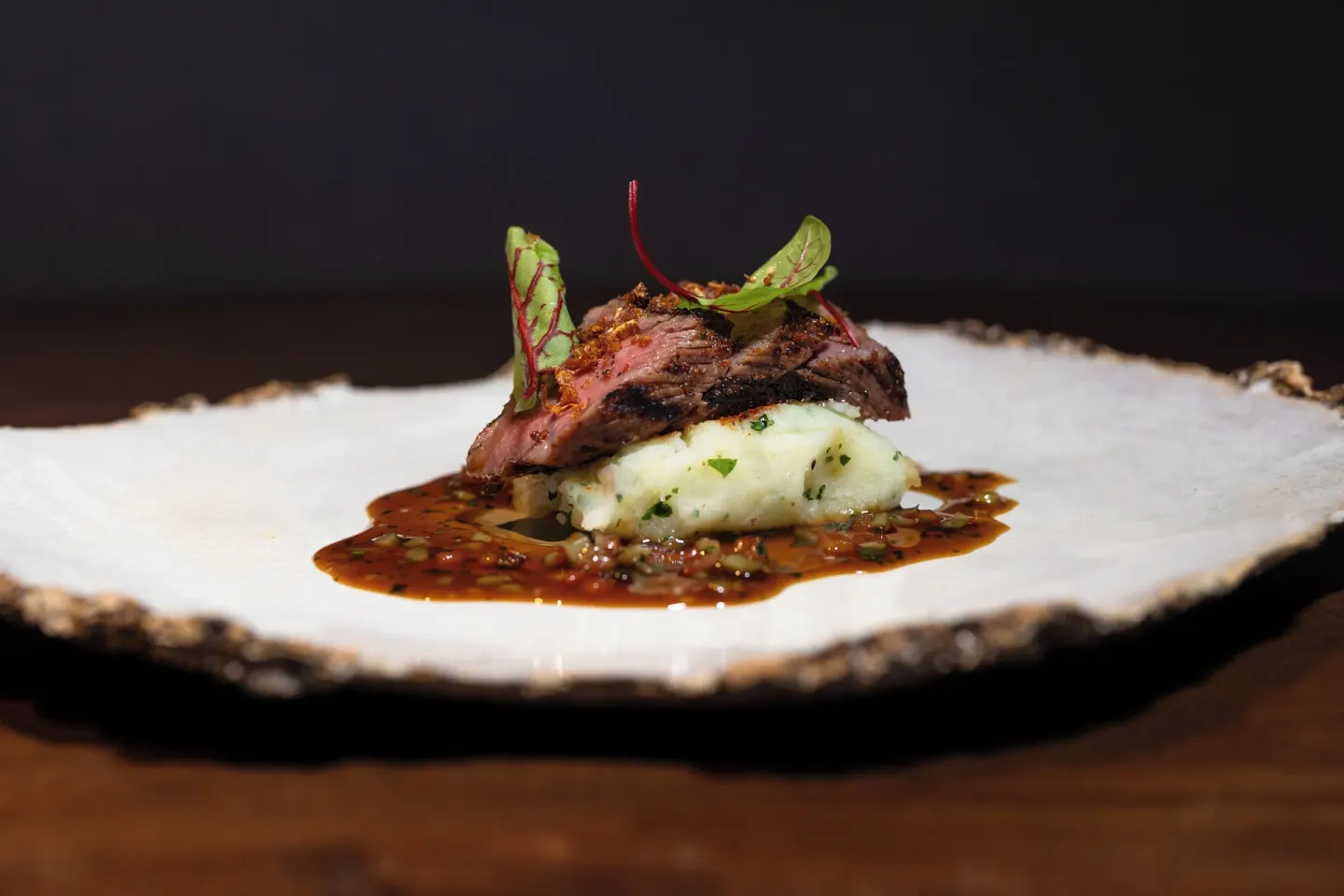 A plated steak entrée with potatoes and sauce is presented at The Kahala Hotel & Resort.