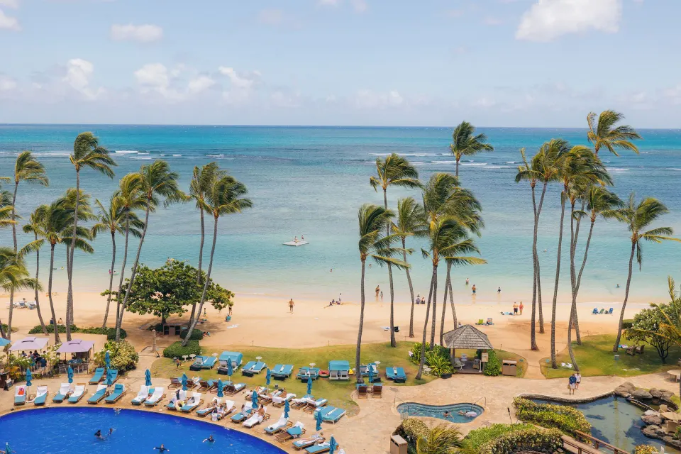 Oceanfront beach, pool loungers, palms, and turquoise water at The Kahala Hotel & Resort.