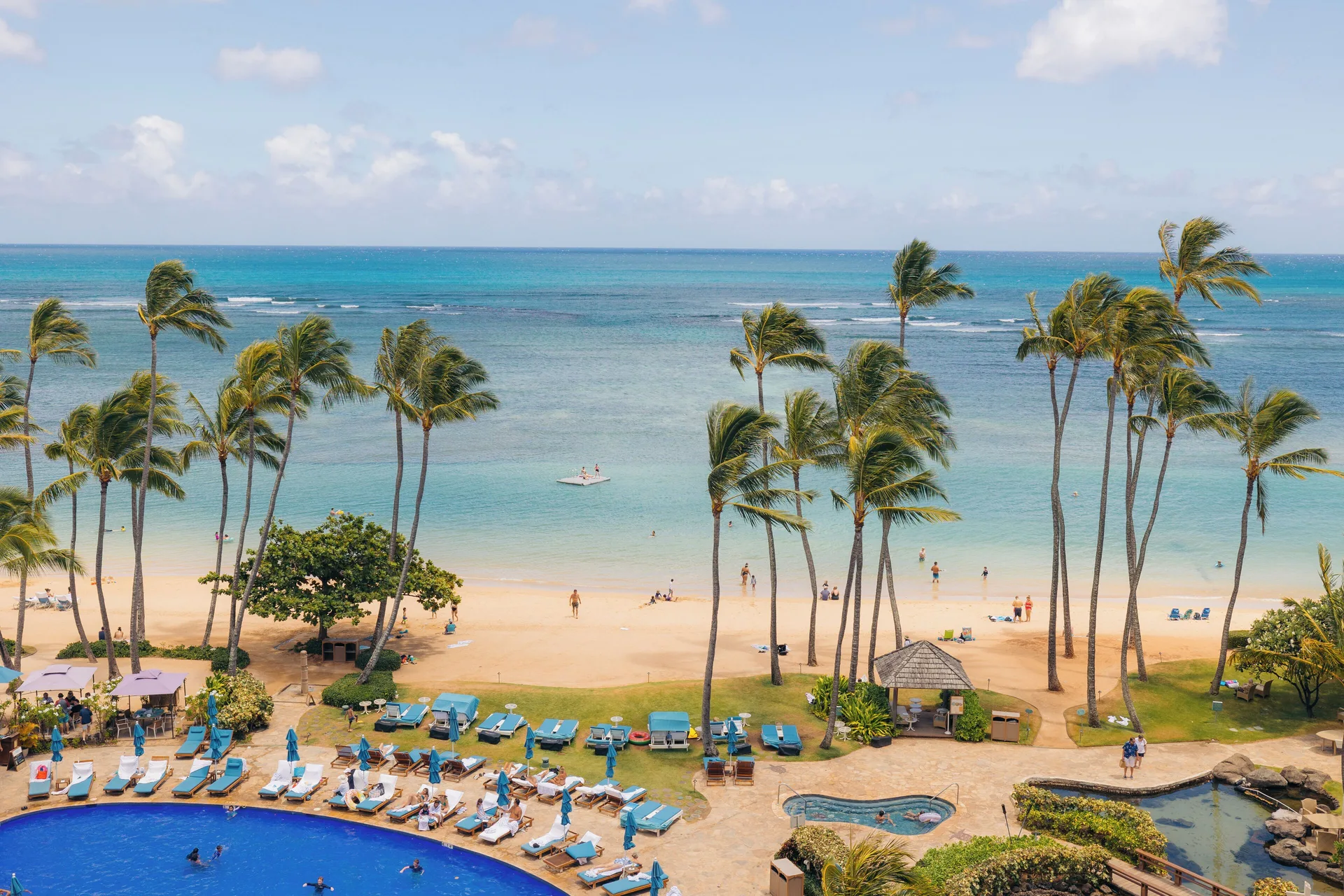Oceanfront beach, pool loungers, palms, and turquoise water at The Kahala Hotel & Resort.
