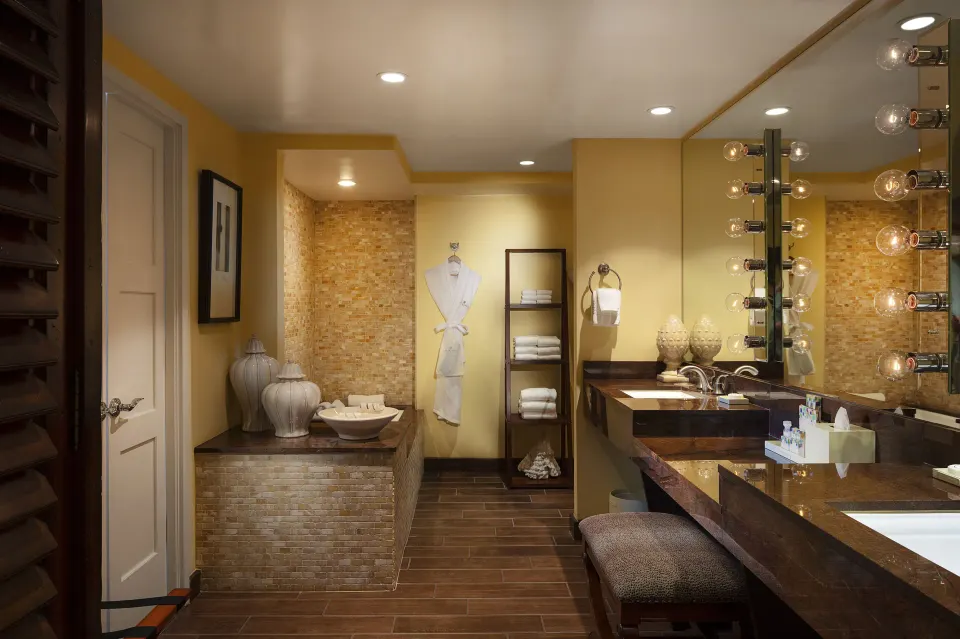 Tower Suite I bathroom vanity with lit mirror, robe, towels, and tub area at The Kahala Hotel & Resort.