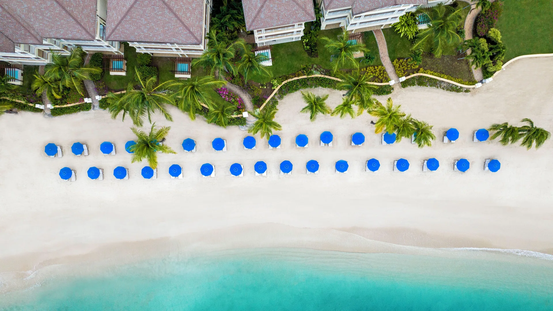 An overhead view shows beach umbrellas, palms, and villas at The Landings Resort & Spa.