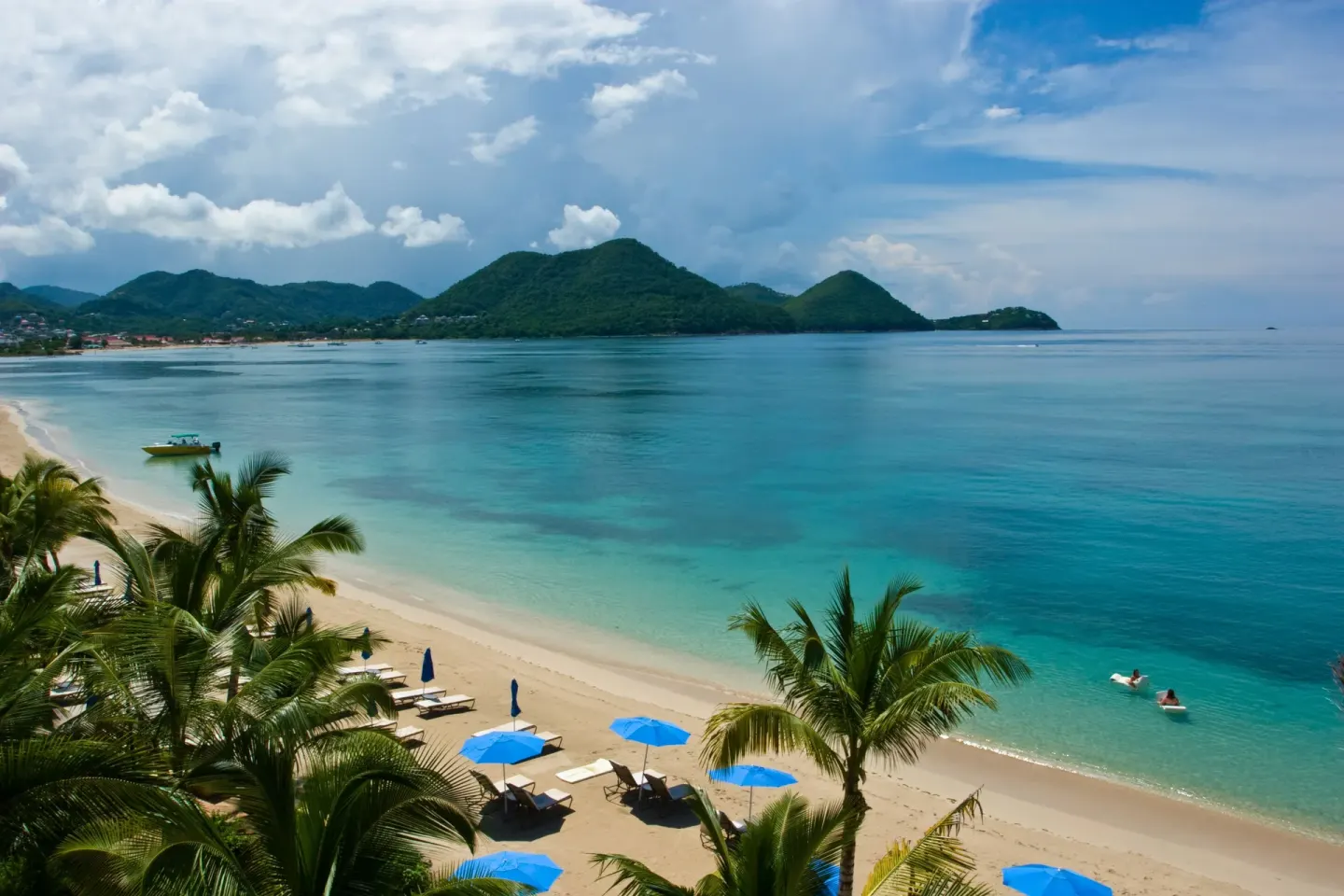 Sandy beach, turquoise water, and green hills are seen from The Landings Resort & Spa.