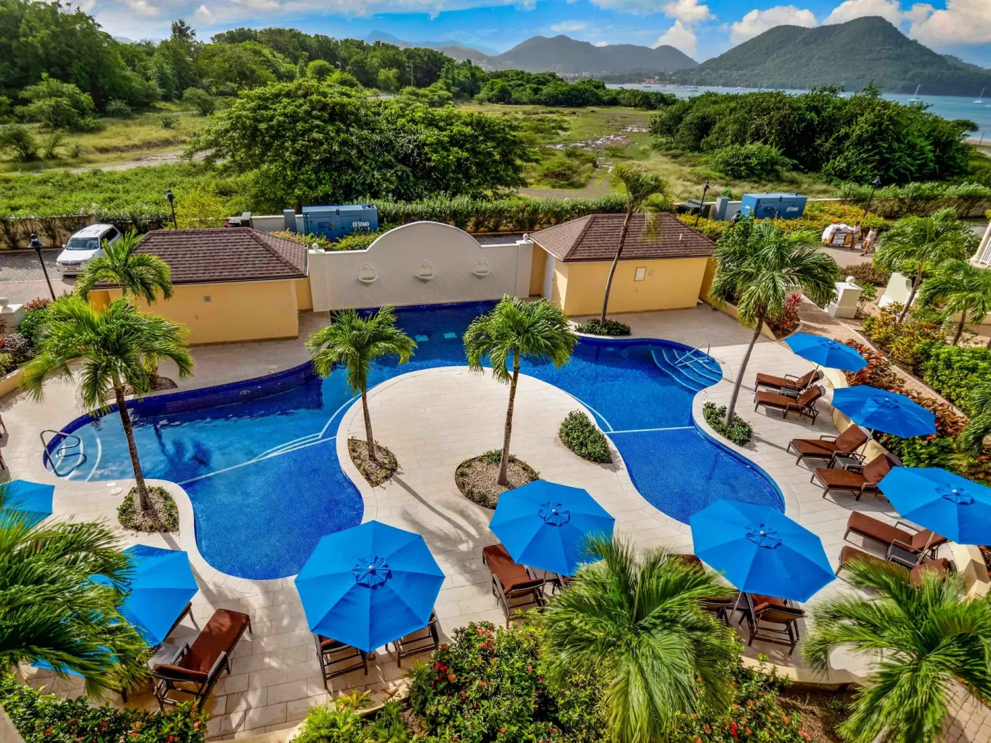Curving pool with blue umbrellas, palms and hills beyond at The Landings Resort & Spa.