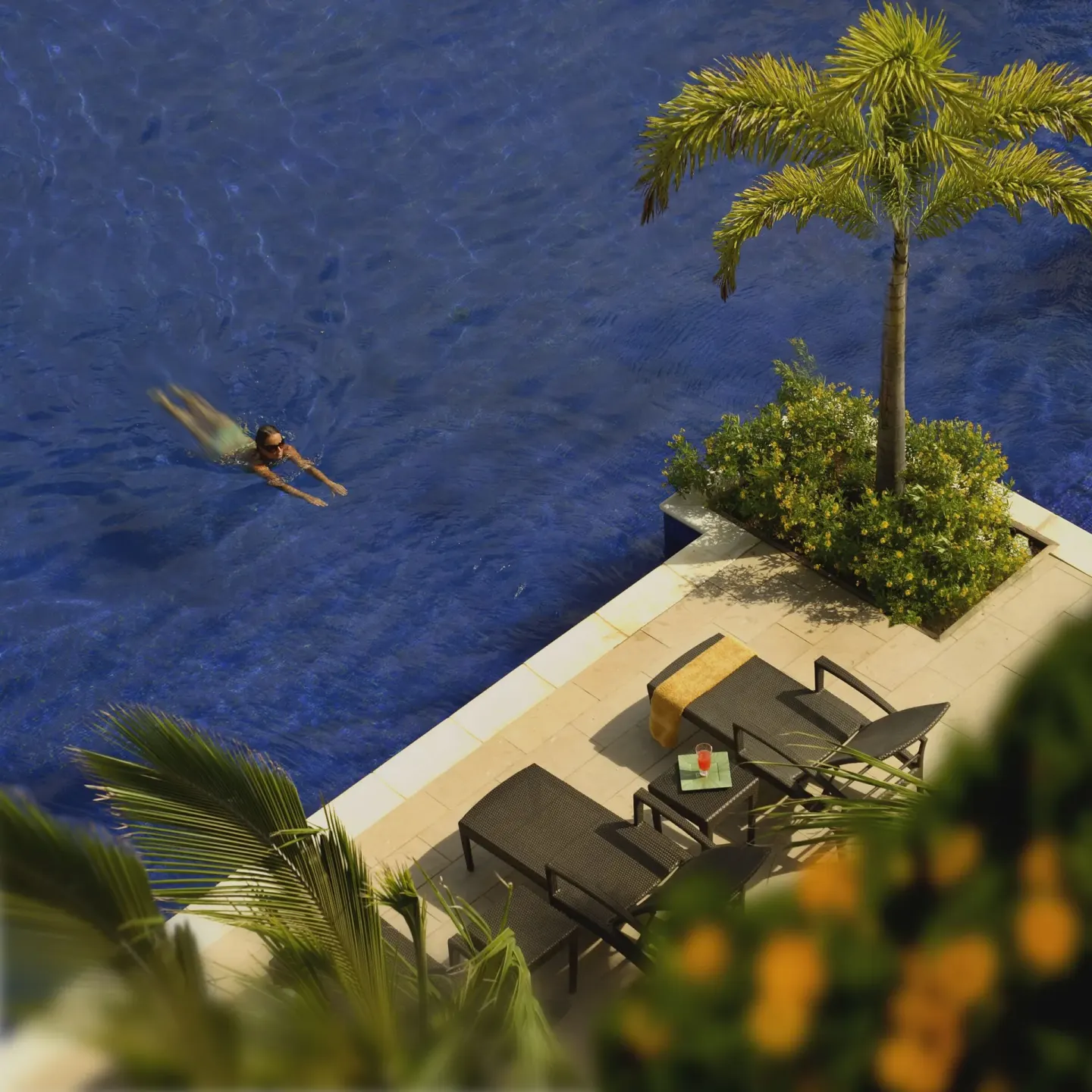 Swimmer in a blue resort pool beside loungers and palms at The Landings Resort & Spa.
