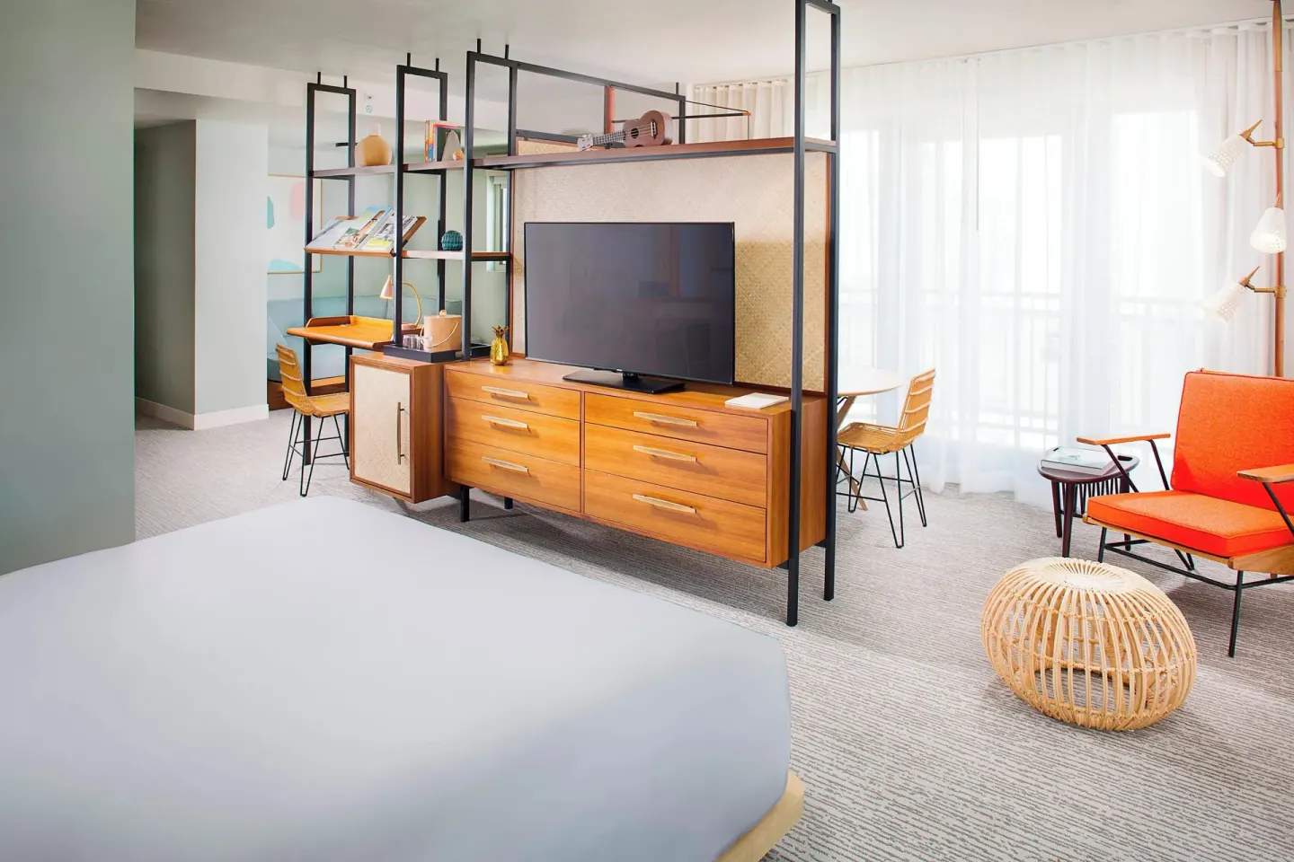 Corner Suite with bed, TV console, desk and orange chair at The Laylow Waikiki, Autograph Collection.