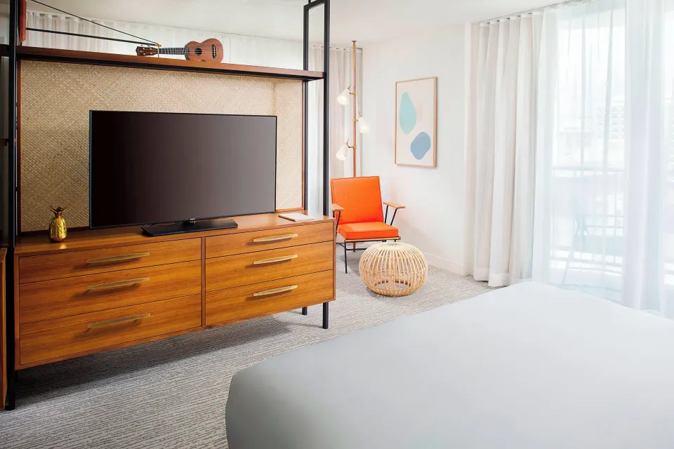 Corner Suite bed, TV console, and balcony curtains at The Laylow Waikiki, Autograph Collection.