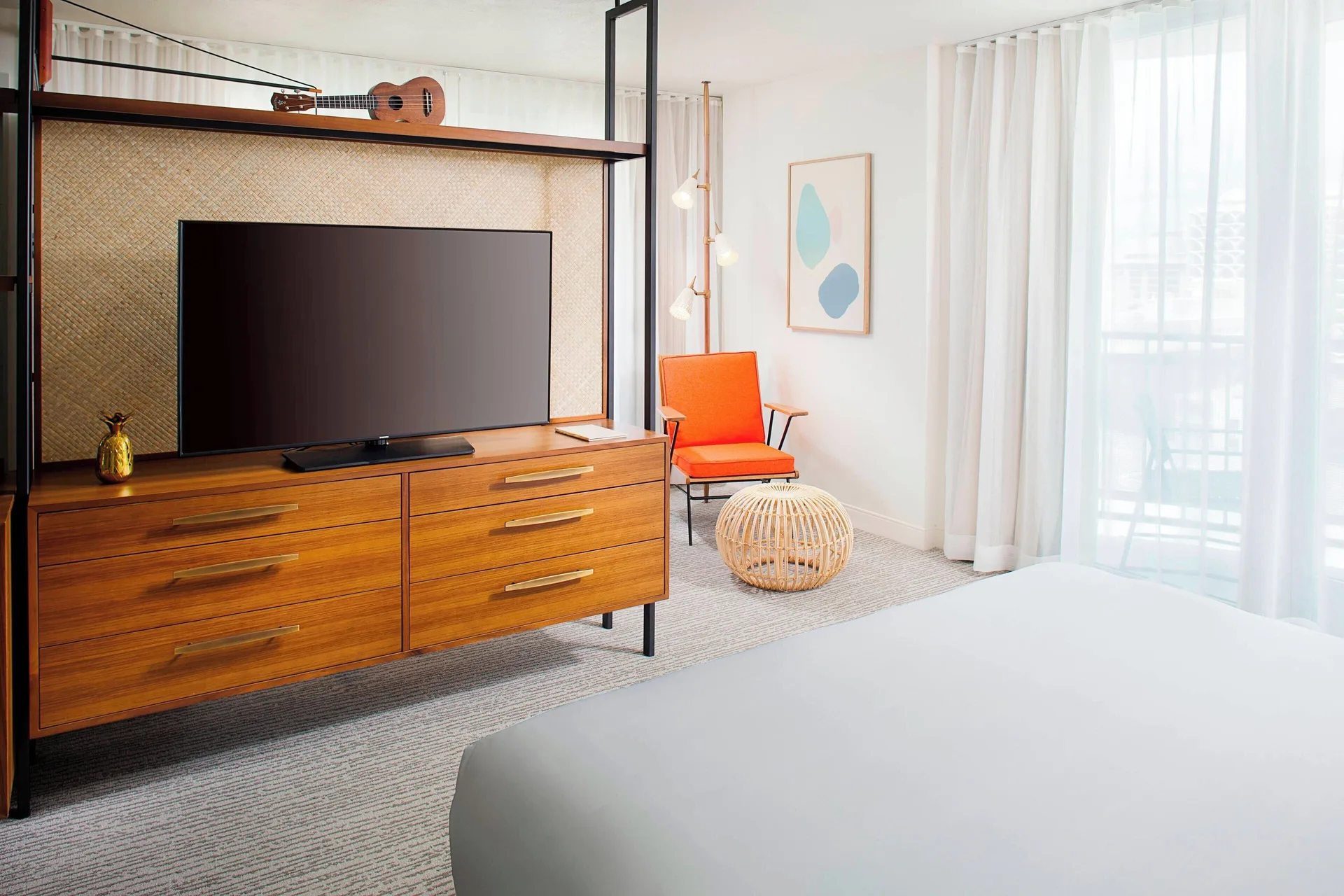 Corner Suite bed, TV console, and balcony curtains at The Laylow Waikiki, Autograph Collection.