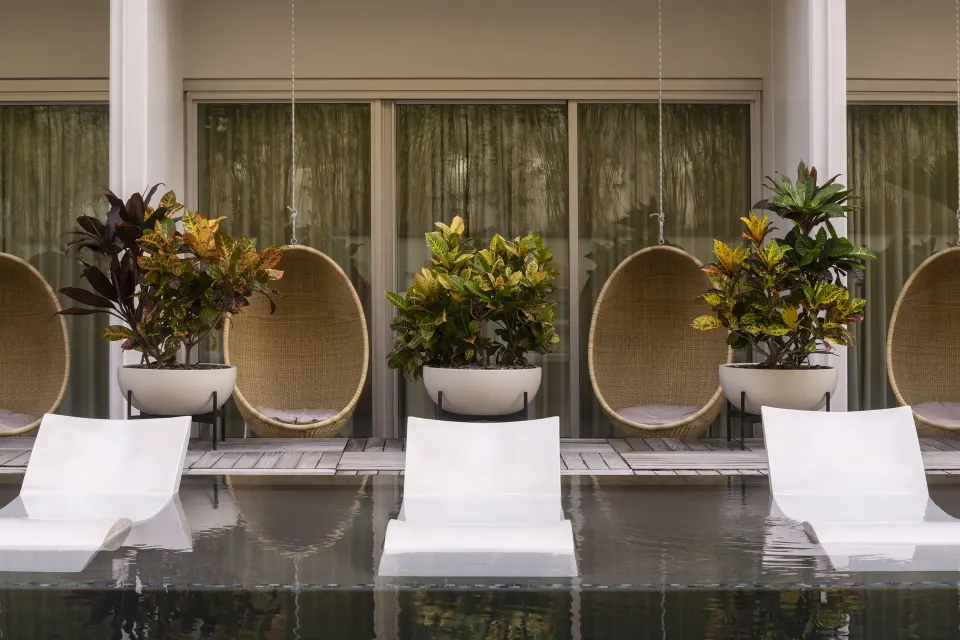 Poolside patio with loungers, planters, and hanging chairs at The Laylow Waikiki, Autograph Collection.