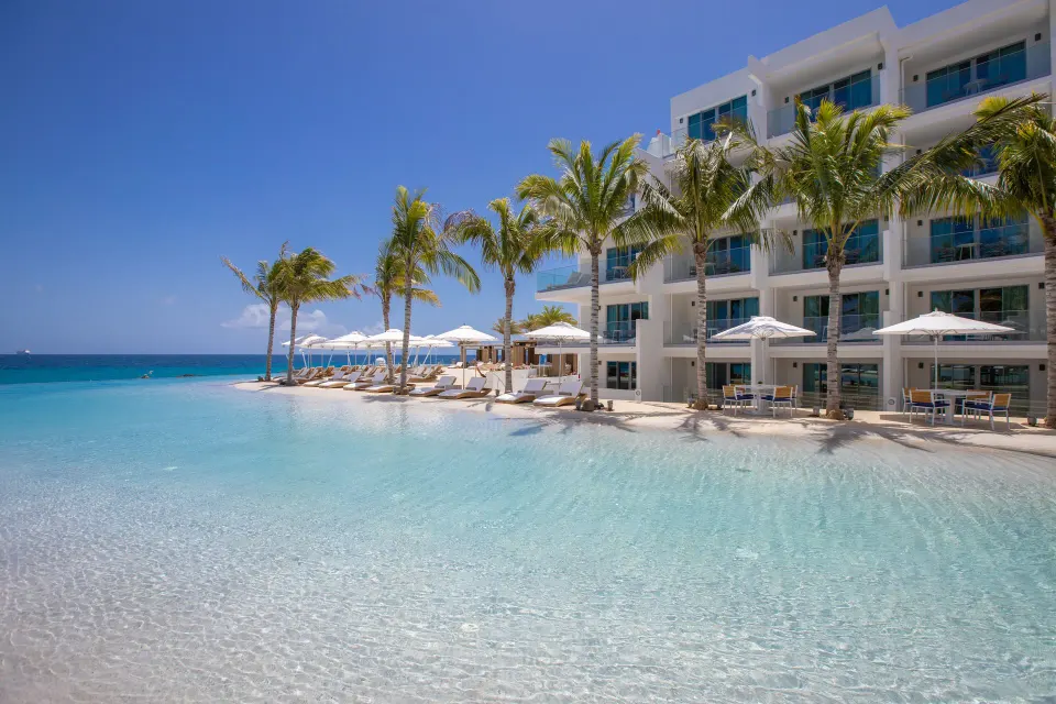 Beachfront pool, palms and white guest room building at The Morgan Resort Spa Village.