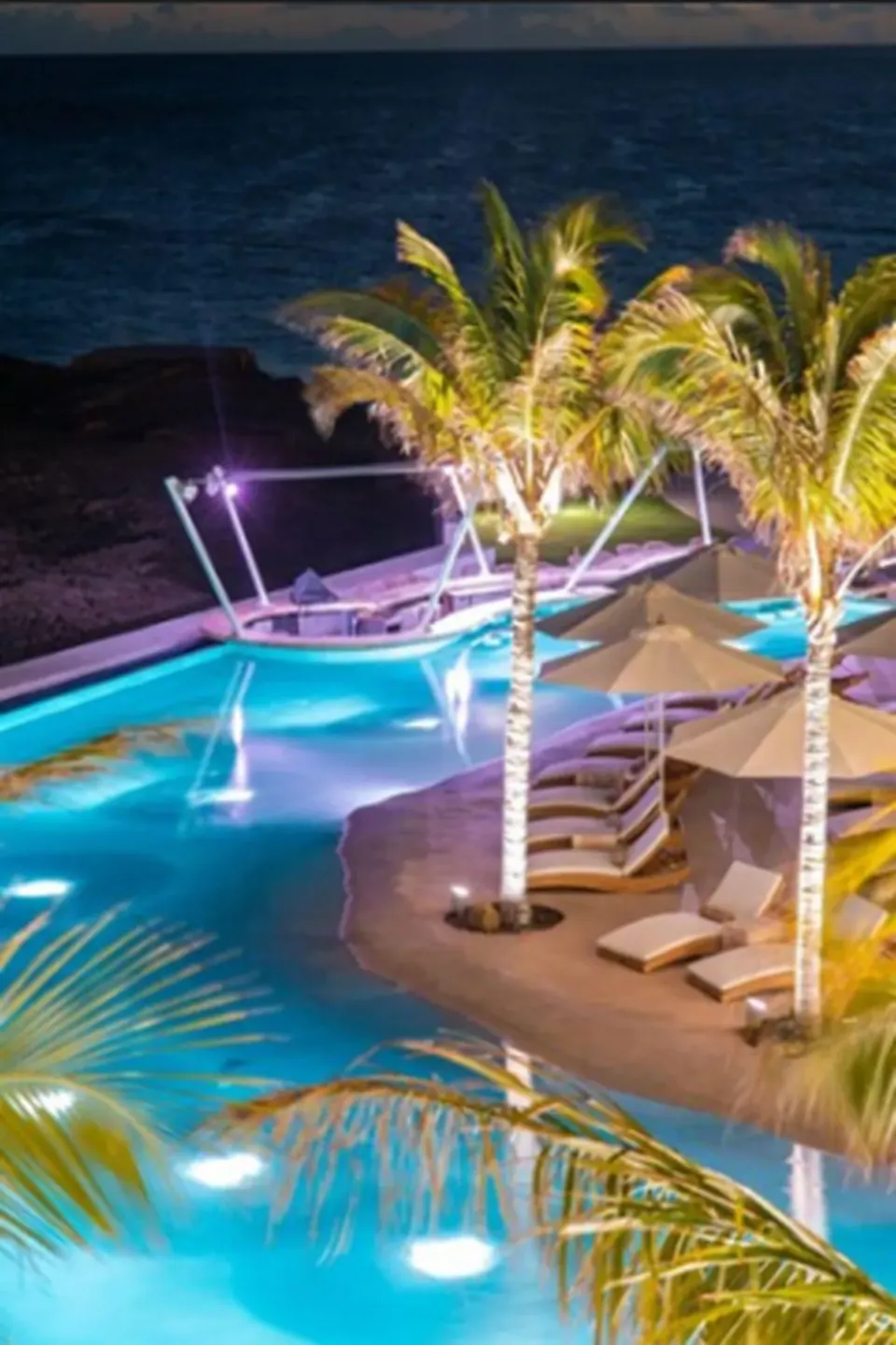 Illuminated pool and palm trees at night at The Morgan Resort Spa Village.