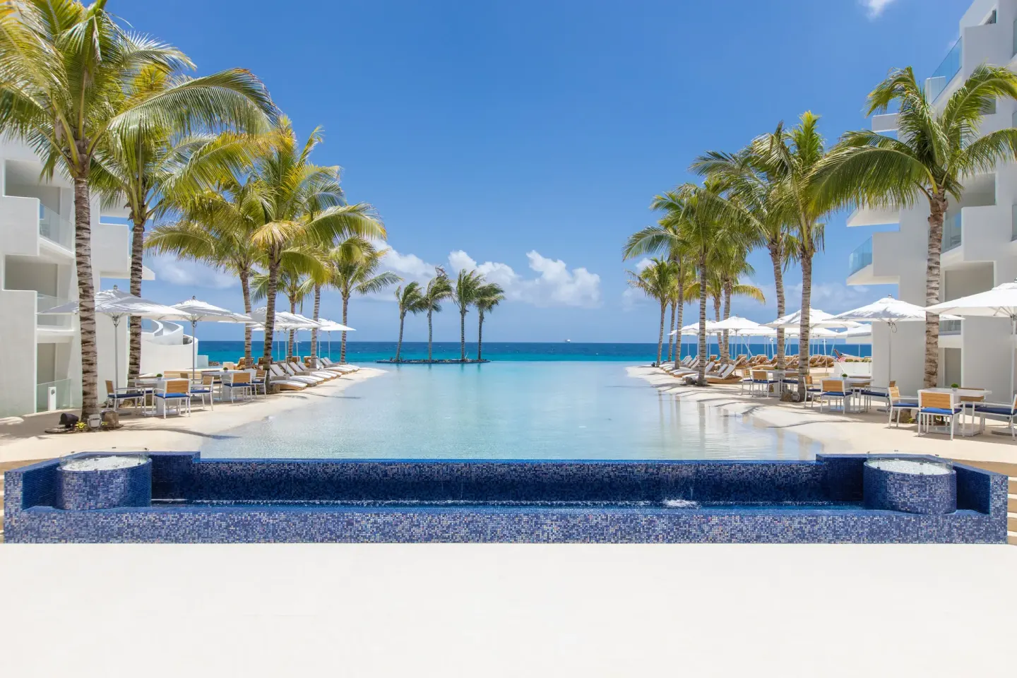 Symmetrical lagoon-style pool framed by palms and white buildings at The Morgan Resort Spa Village.