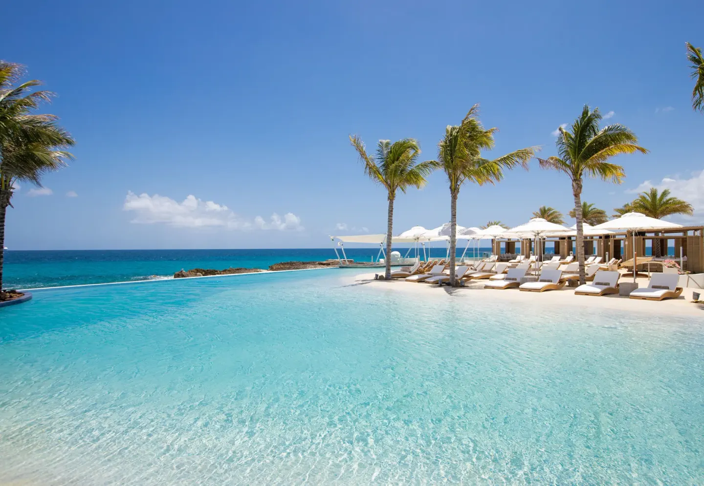 Wide oceanfront pool with palm trees and sun loungers at The Morgan Resort Spa Village.